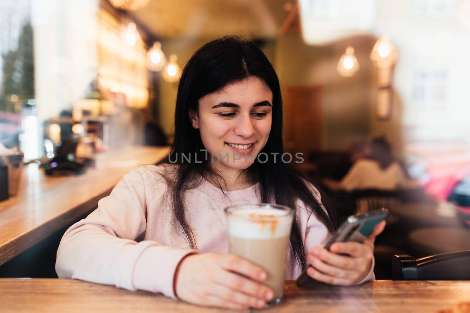 Girl smiling, drinks coffee in cafe and reading phone. Blurred background. High quality photo