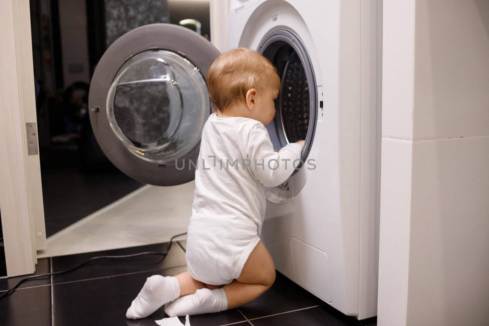 Child climbing into front-loading washing machine. Side view. Lack of parental supervision.