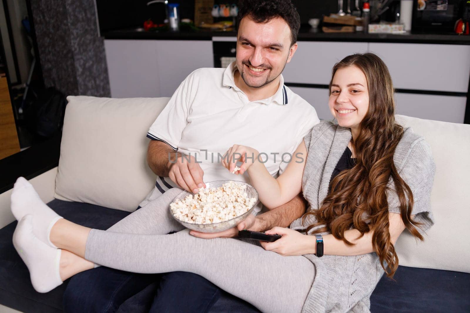Happy couple eating popcorn and watching tv at home.
