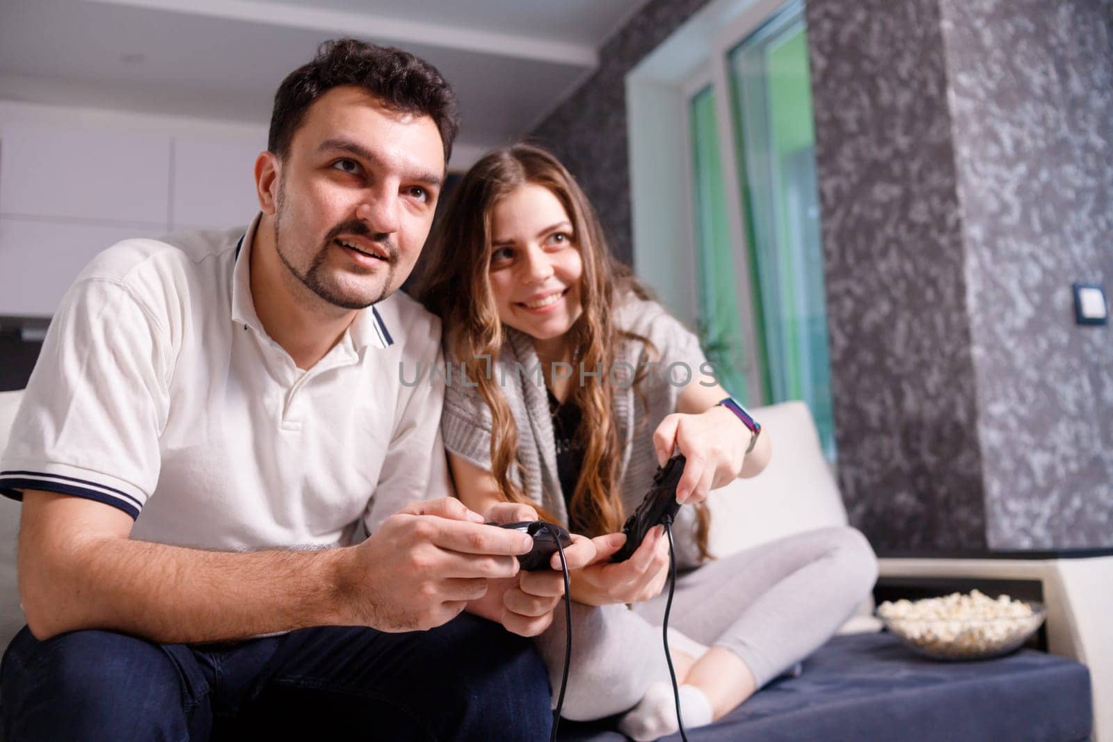 Young couple playing video games sitting on sofa in livingroom at home.
