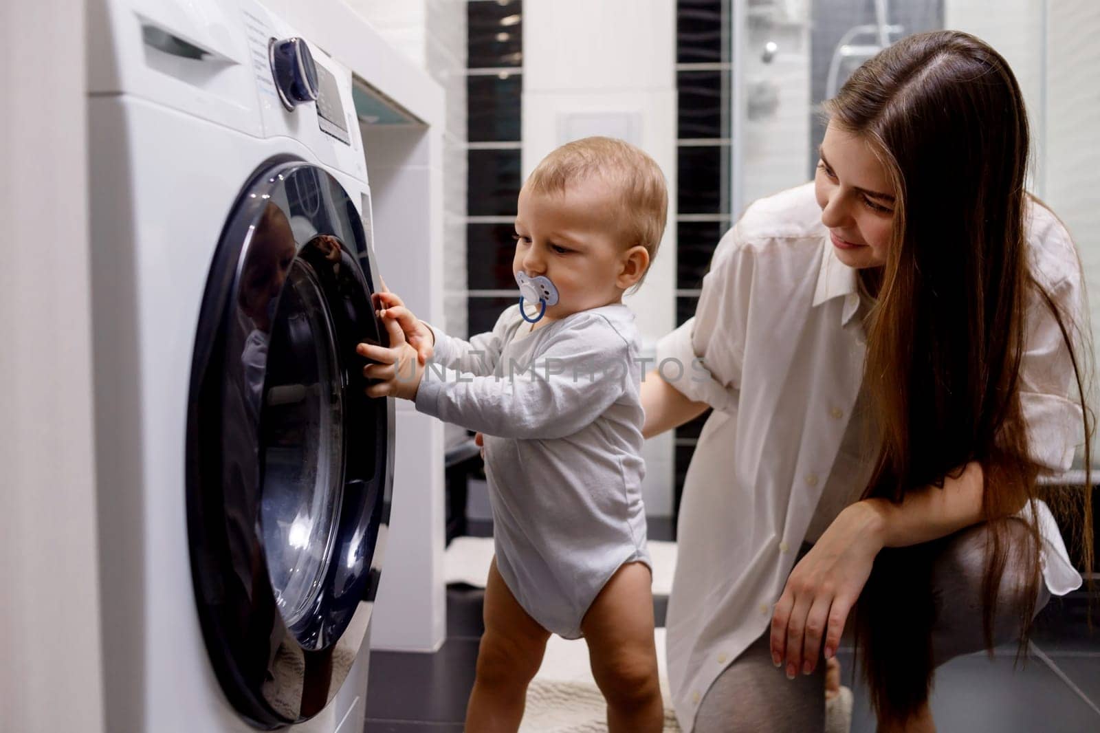 Woman with infant child using washing machine at home.