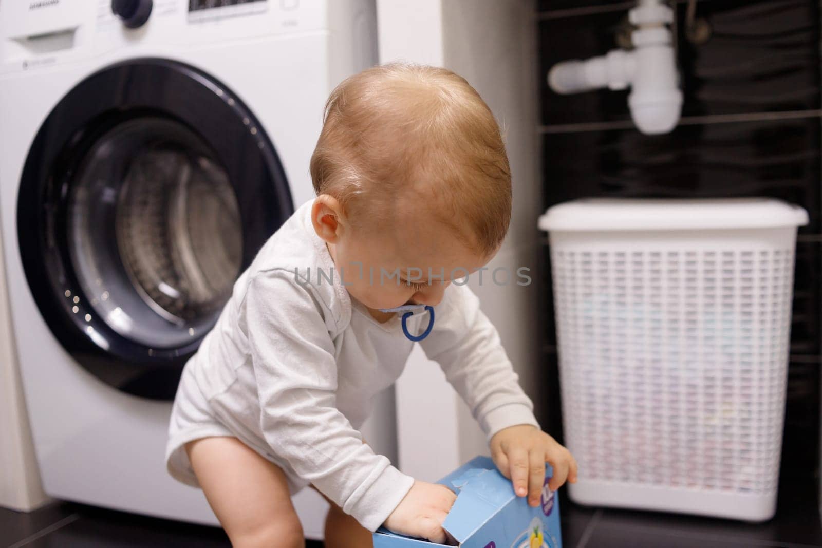 Infant boy open box with tablet for dishwasher or detergent in bathroom alone. Children without parental supervision