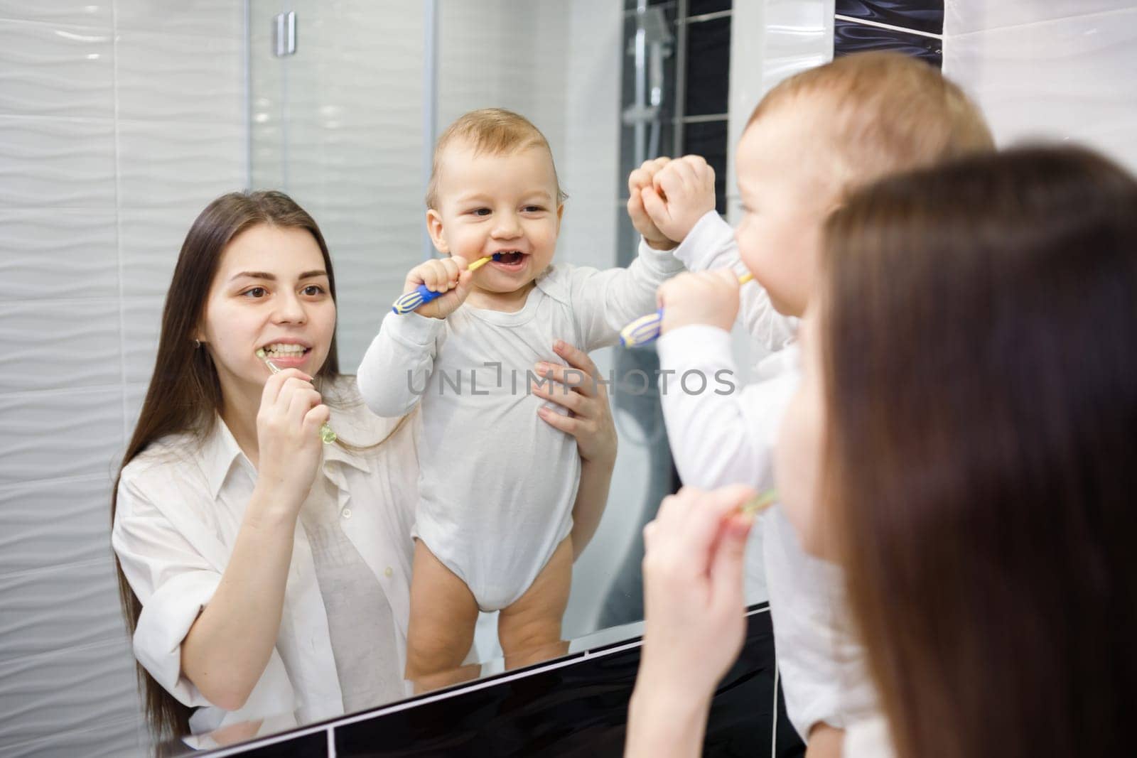 Young caucasian mother teaching baby boy how to brush teeth with toothbrush.