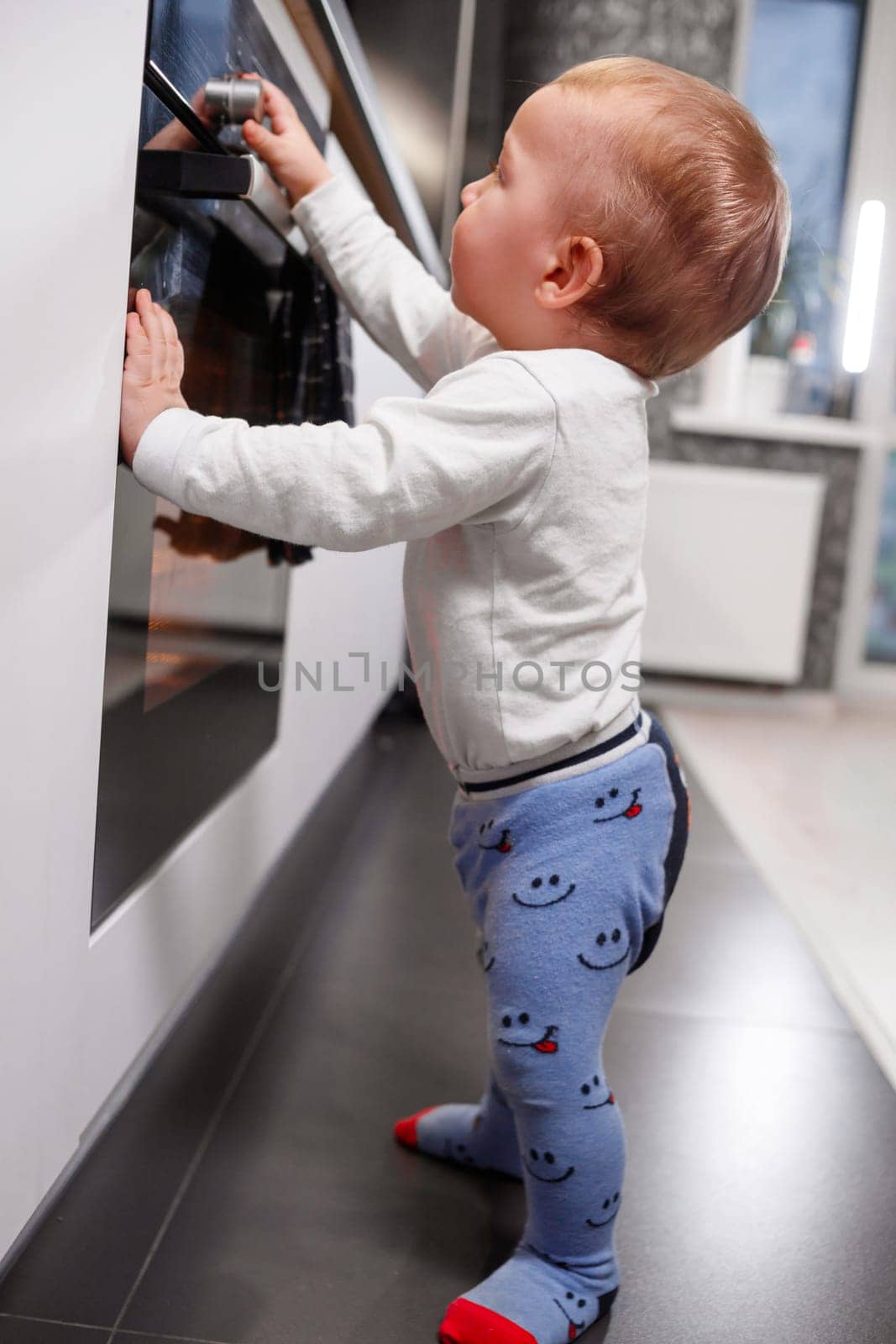 Little child playing with electric stove in kitchen