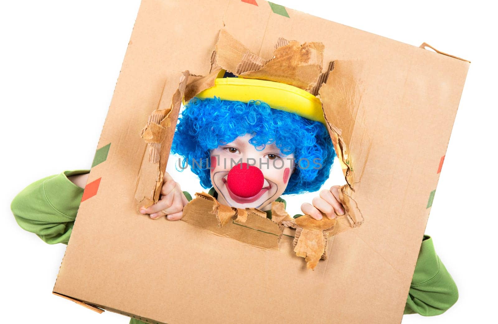 young child dressed as a clown with wig and fake nose has fun watching from the open cardboard