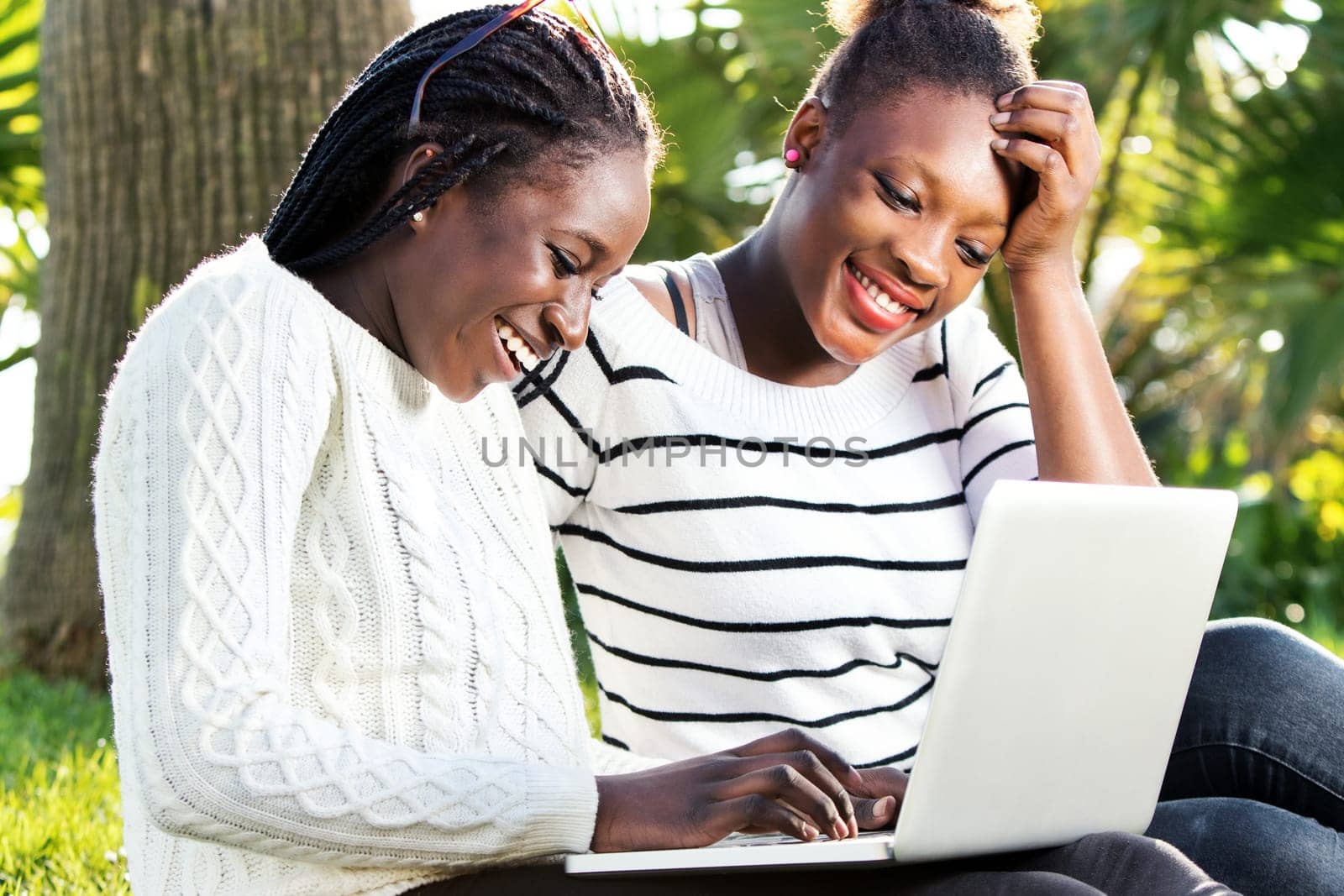 Close up outdoor portrait of two afro american teen girls socializing on laptop in park.