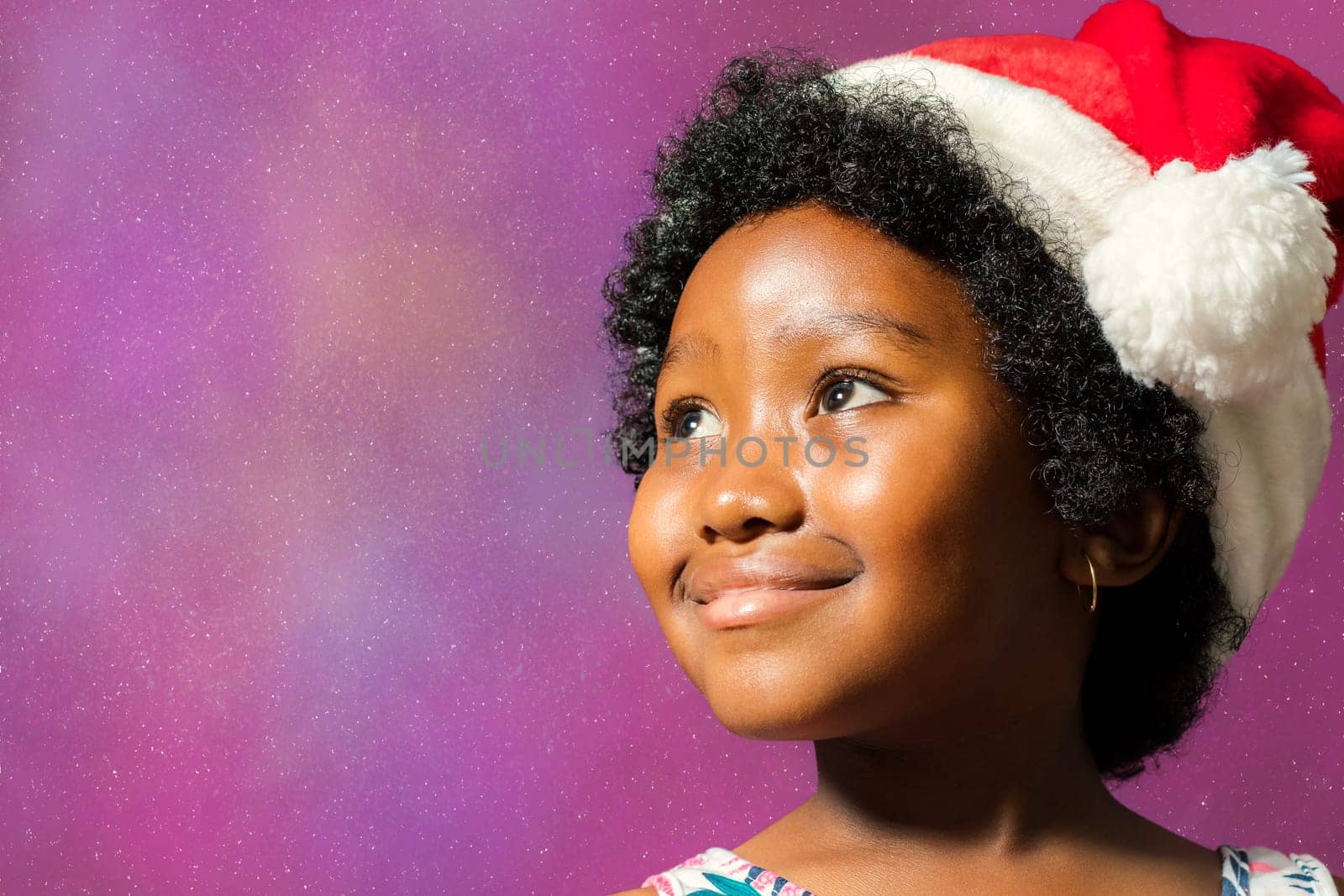 Close up face shot of little african girl wearing christmas hat. Kid staring at upper corner against starburst background.