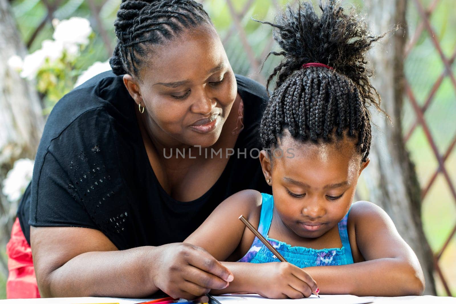 Close up portrait of african teacher supervising little kid doing homework outdoors.