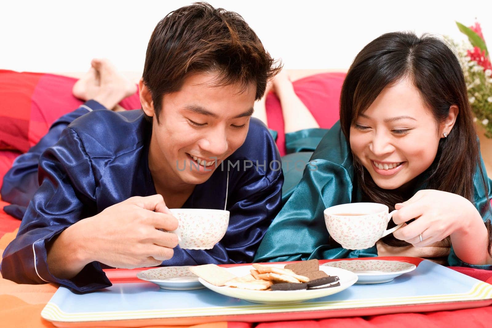 Close-up of a mid adult man holding a cup and lying on the bed with a young woman