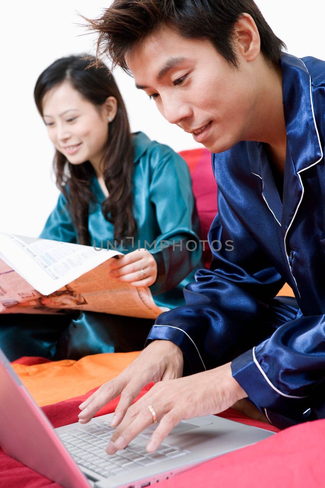 Close-up of a mid adult man using a laptop and young woman reading a newspaper
