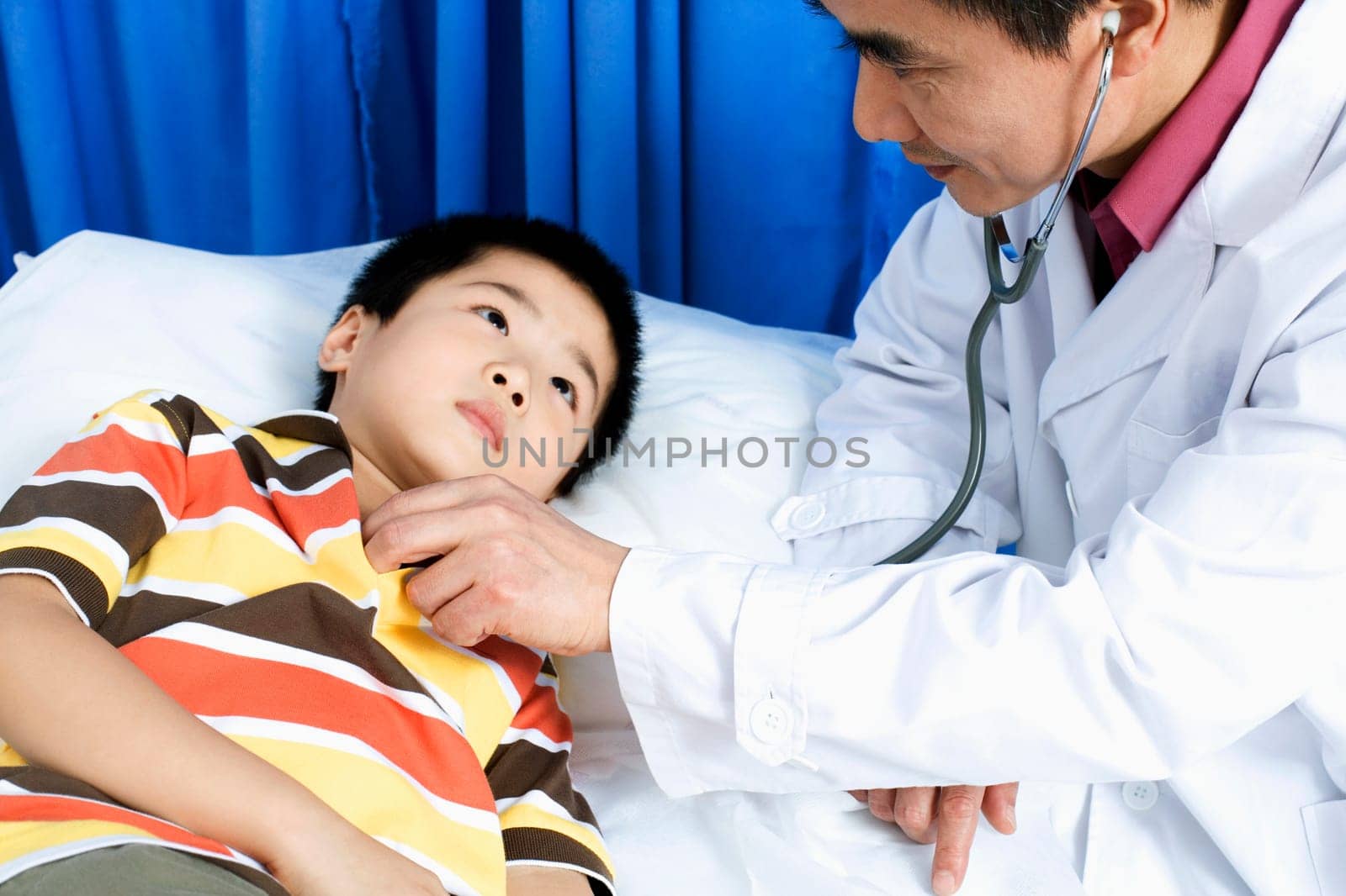 Side profile of a male doctor examining a boy with a stethoscope