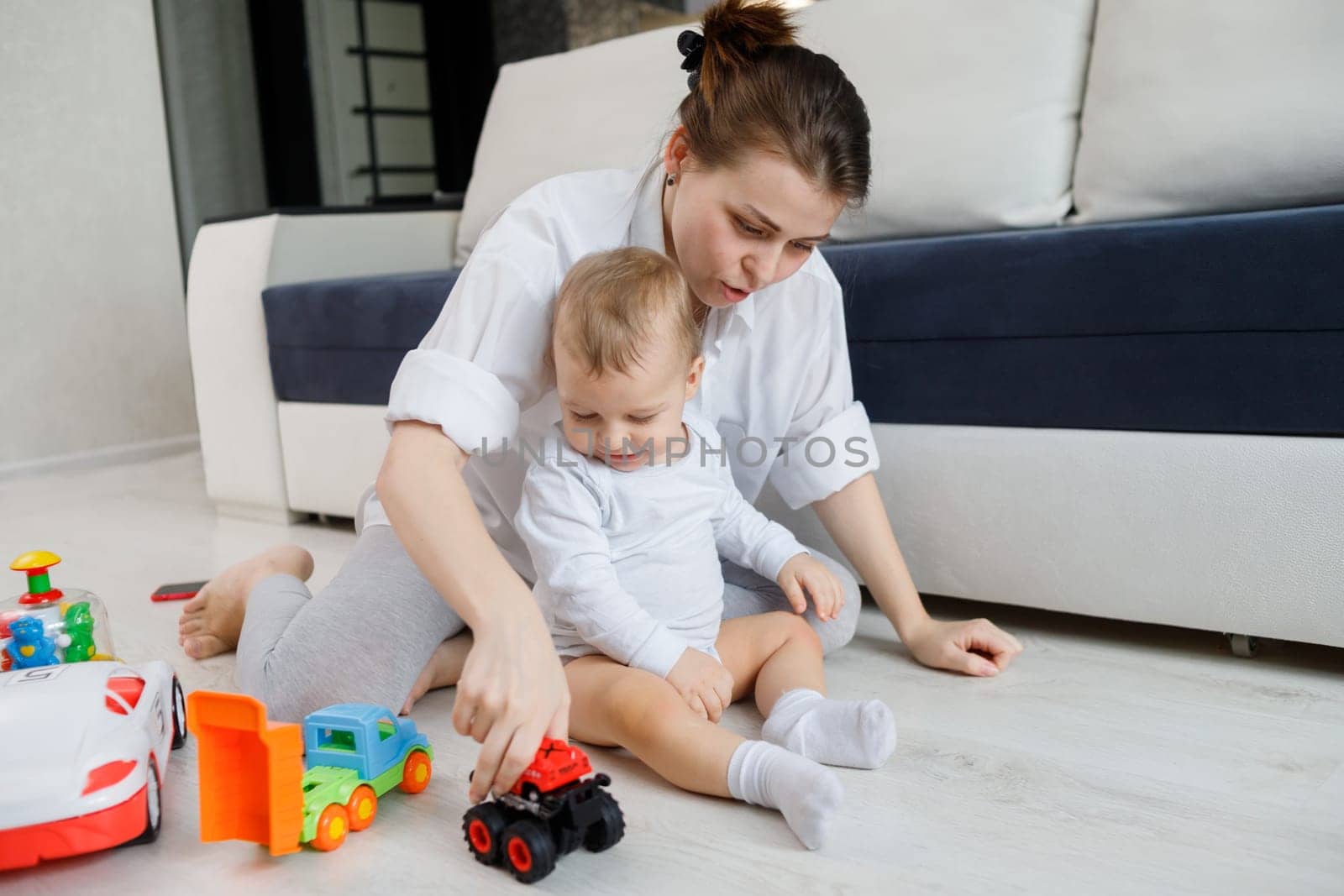 Young mom and little child plays with toys sitting on floor.