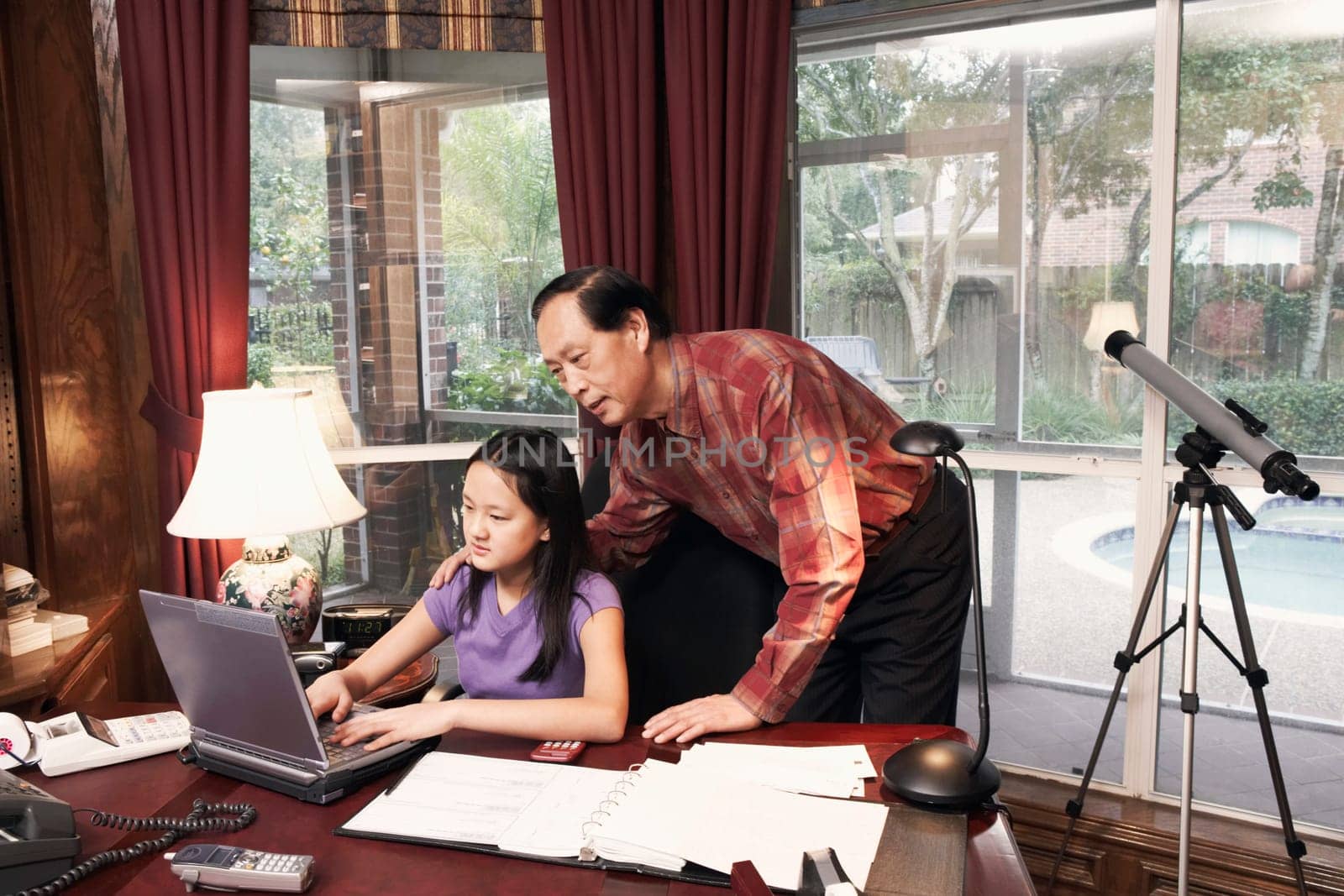 Girl using a laptop with her grandfather standing beside her
