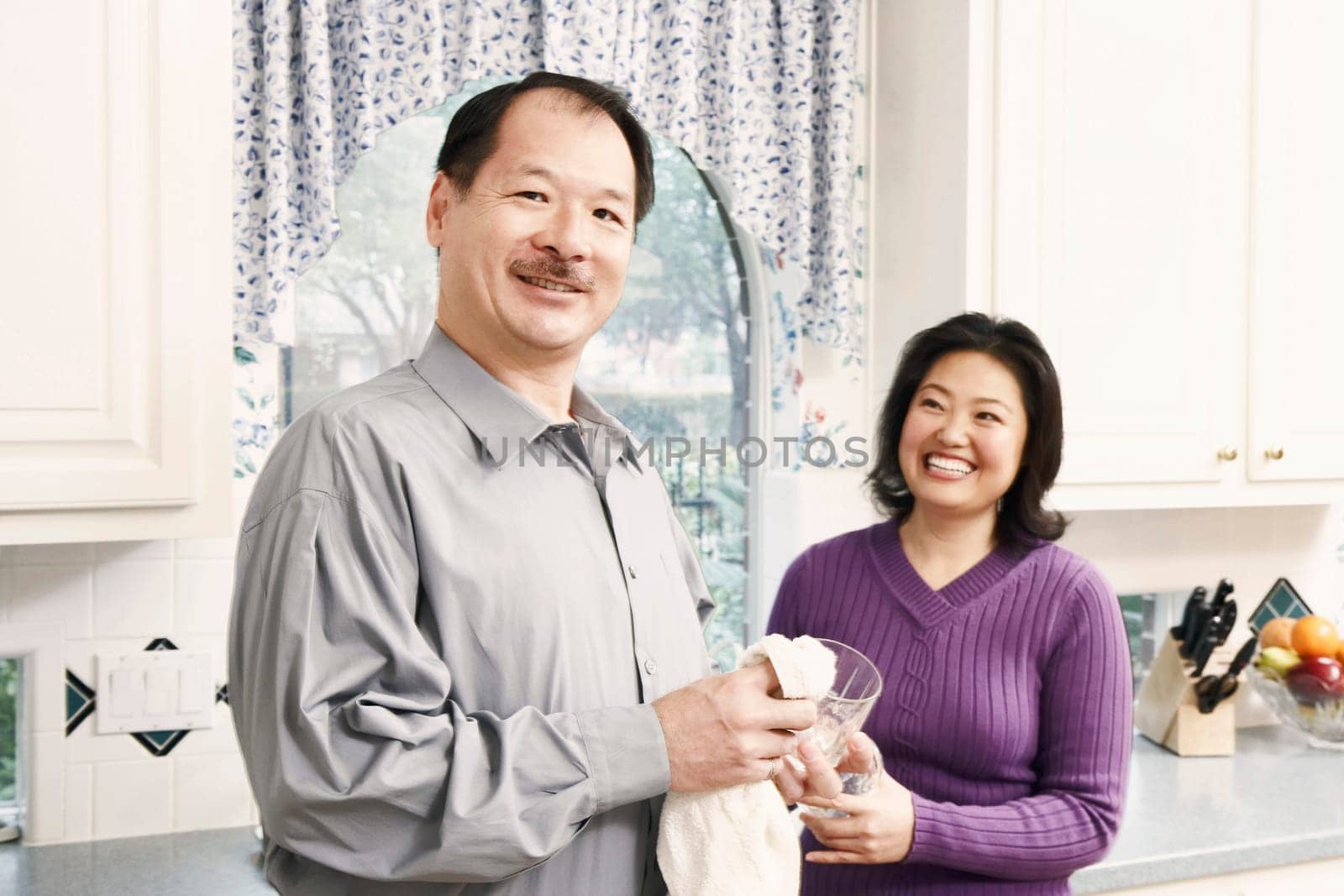 Portrait of a senior man cleaning a glass with a mature woman standing behind her