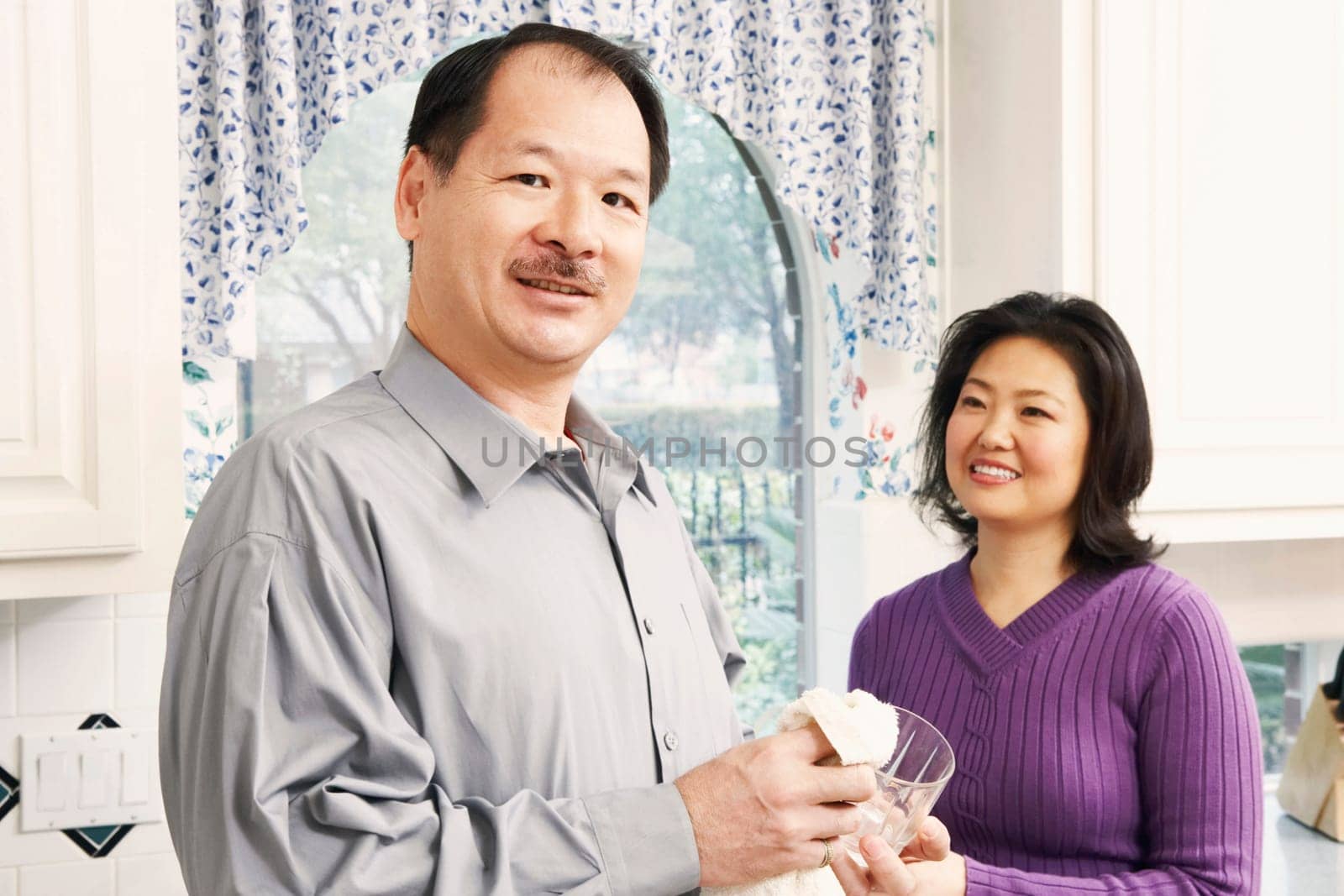 Portrait of a senior man cleaning a glass with a mature woman standing behind him