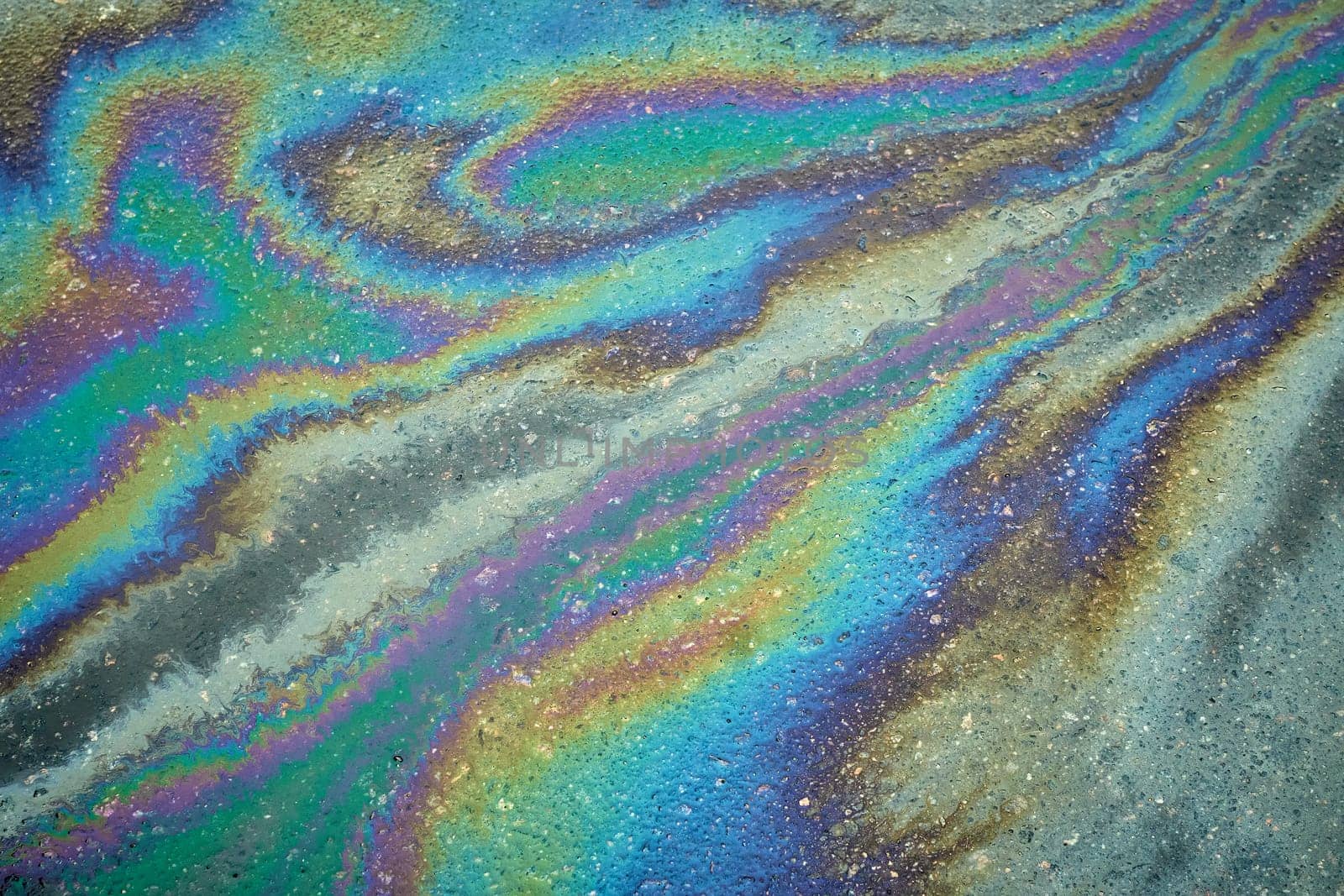 Vivid patterns created by an oil slick on the asphalt underscore the effects of rain in urban landscapes, raising awareness about the challenges of environmental pollution