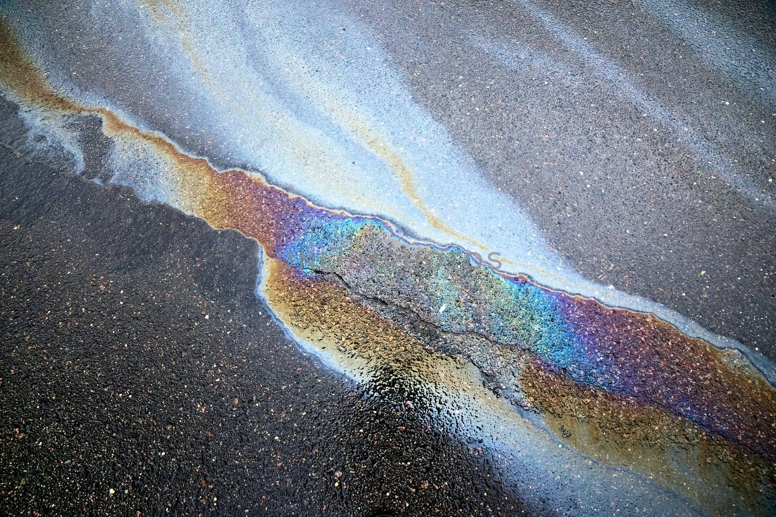 A brightly colored gasoline or oil spill creates a colorful sheen on a cracked asphalt surface