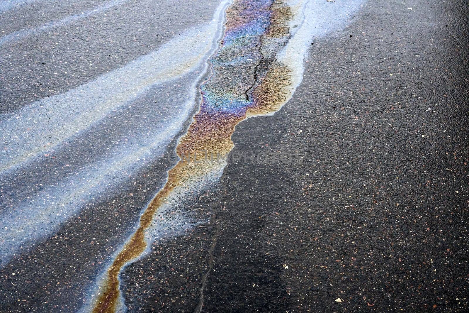 A rainbow colored oil spill creates a striking rainbow effect on a damaged asphalt surface.