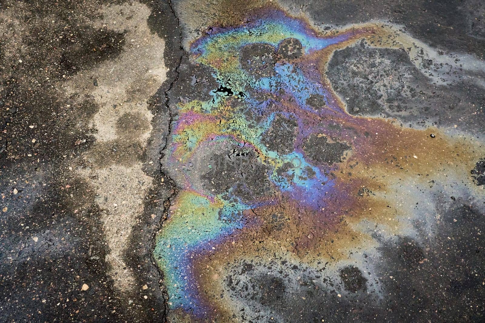 A shimmering gasoline spill creates a vibrant rainbow on asphalt, raising awareness of environmental pollution