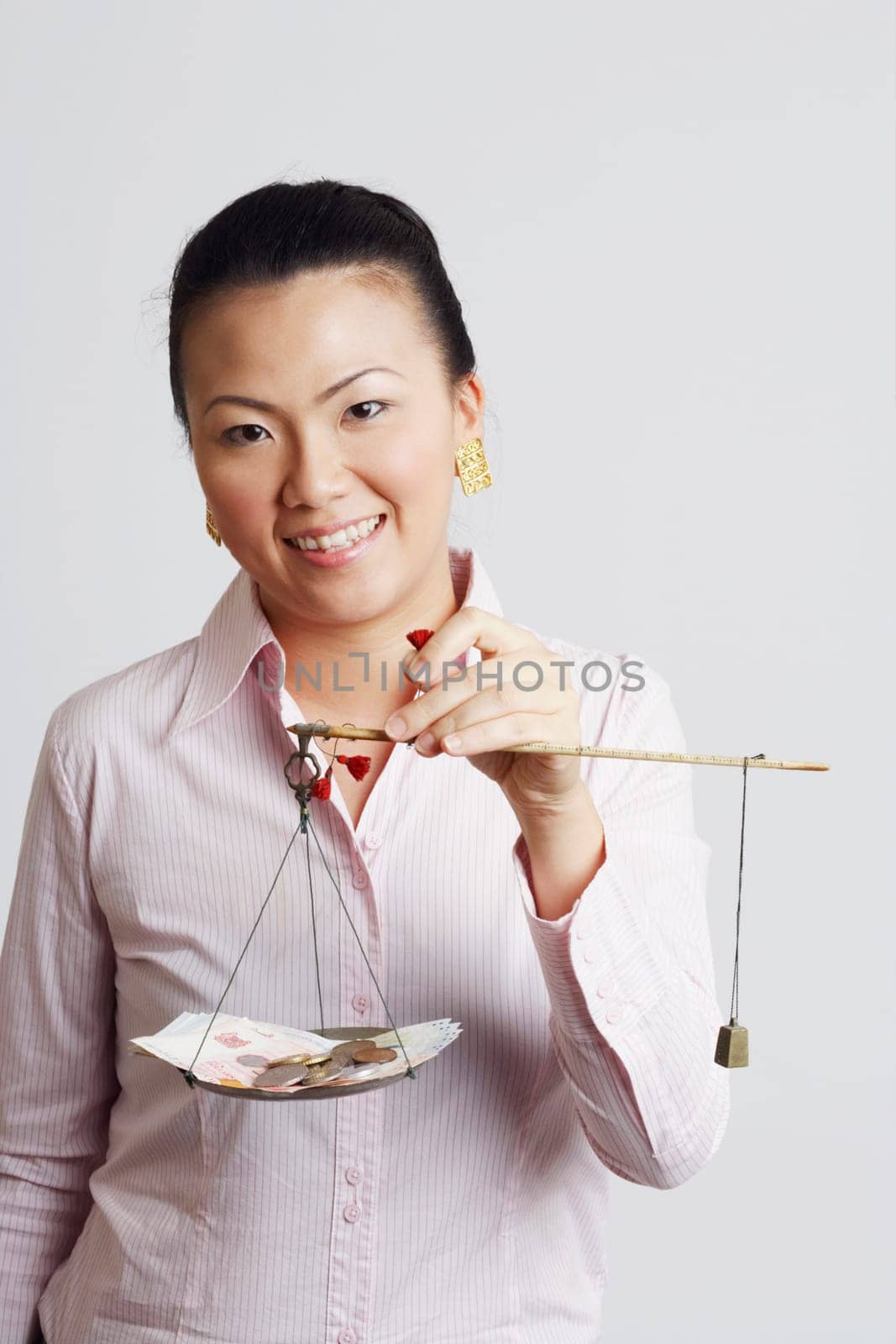 Portrait of a businesswoman weighing paper currency with coins on a weighing scale and smiling