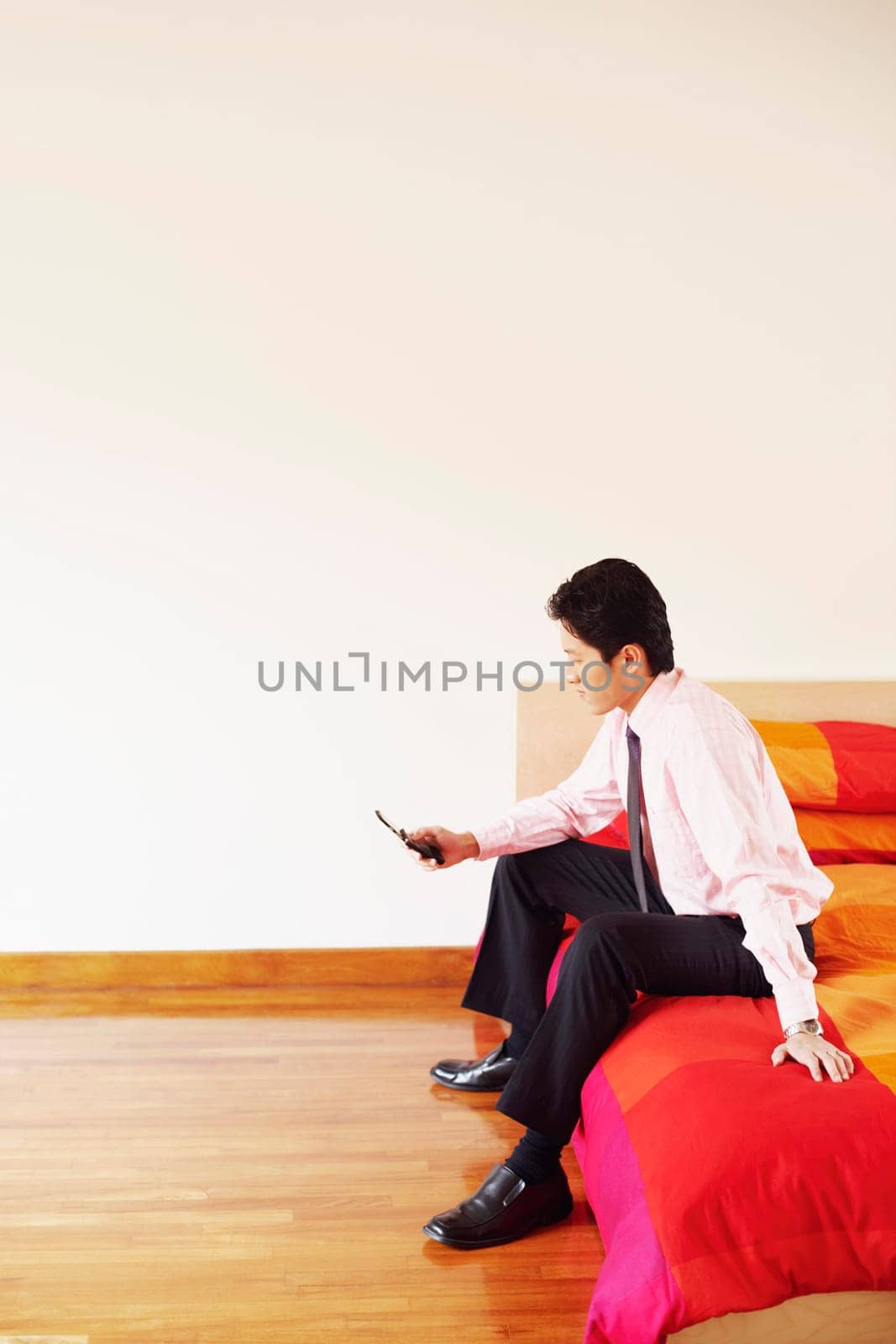 Side profile of a businessman sitting on the bed and operating a mobile phone