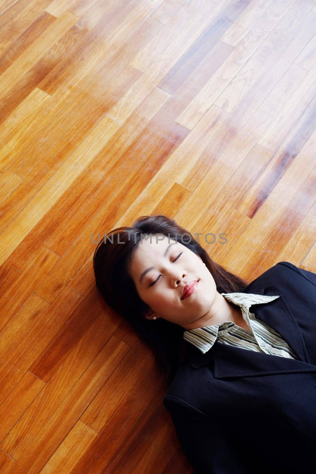 High angle view of a businesswoman lying on the hardwood floor with her eyes closed