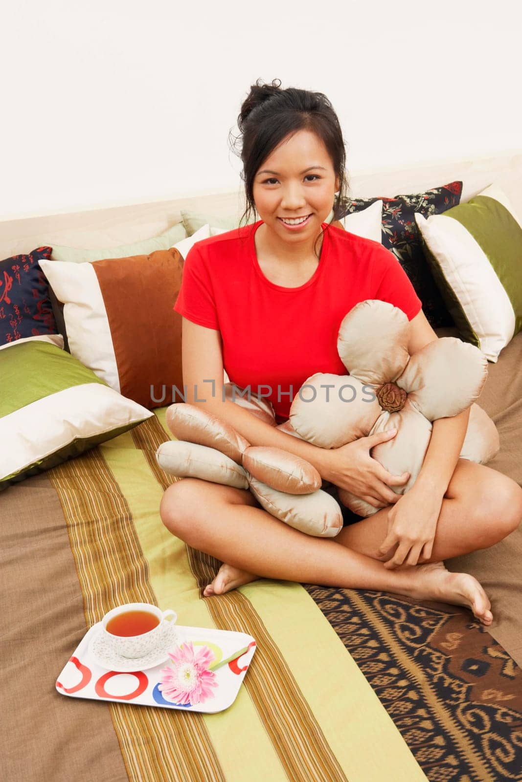 Portrait of a young woman sitting on the bed with cushions and smiling