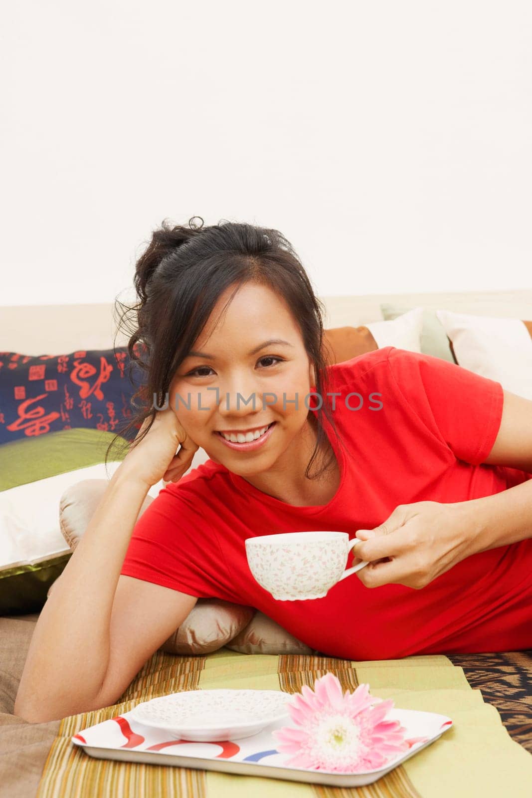 Portrait of a young woman lying on the bed and holding a cup of tea