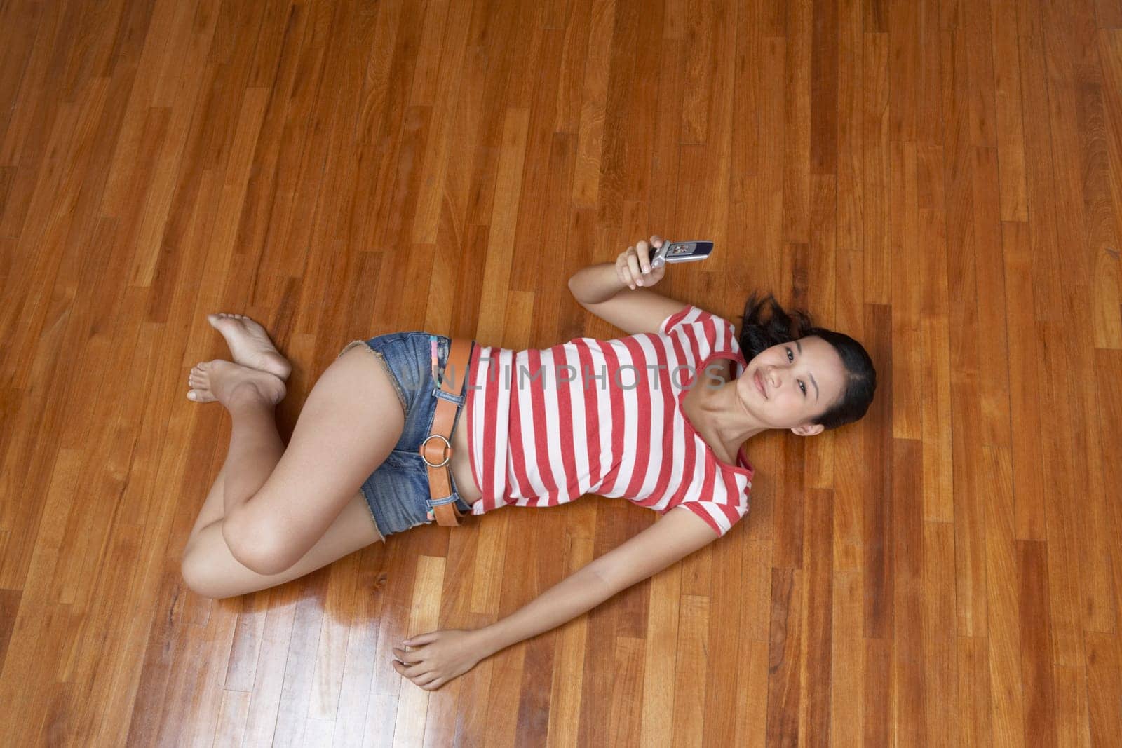 Portrait of a young woman lying on a hardwood floor and holding a mobile phone