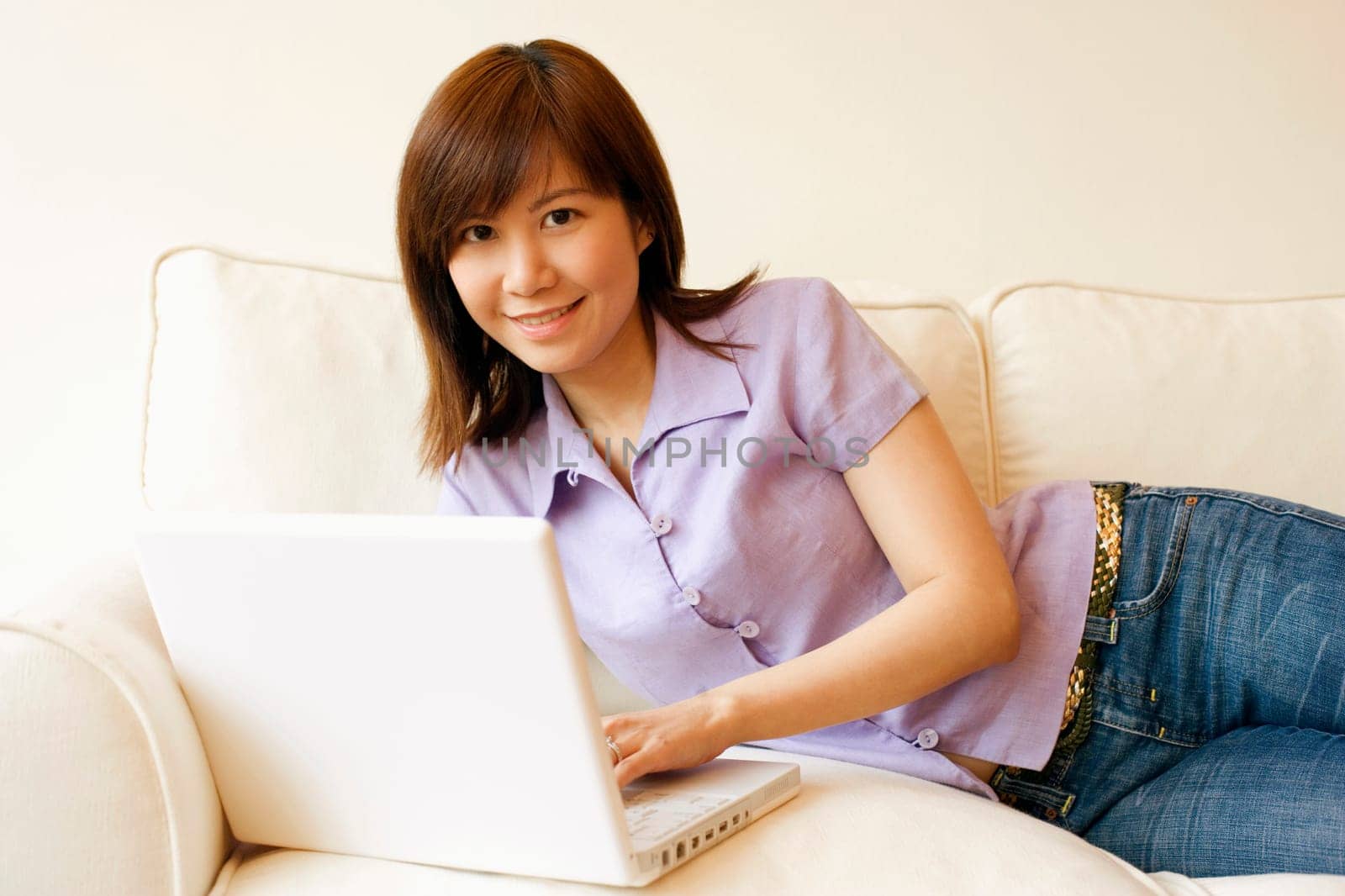 Portrait of a young woman lying on a couch and working on a laptop