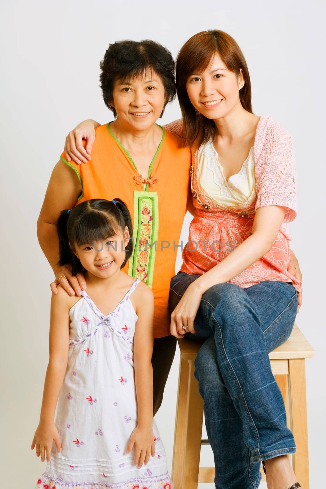 Portrait of a young woman sitting on a stool with her mother and her daughter standing beside her