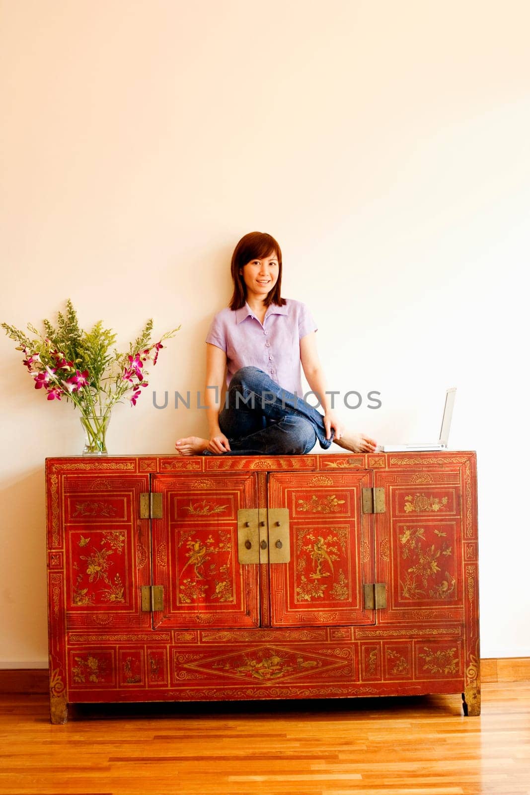 Portrait of a young woman sitting on a cabinet with a laptop beside her