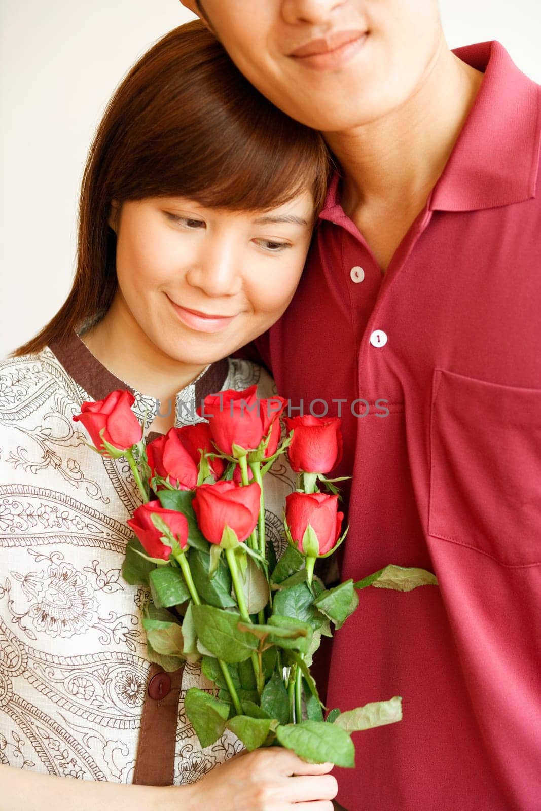 Close-up of a young woman holding a bouquet of red roses and standing with a young man