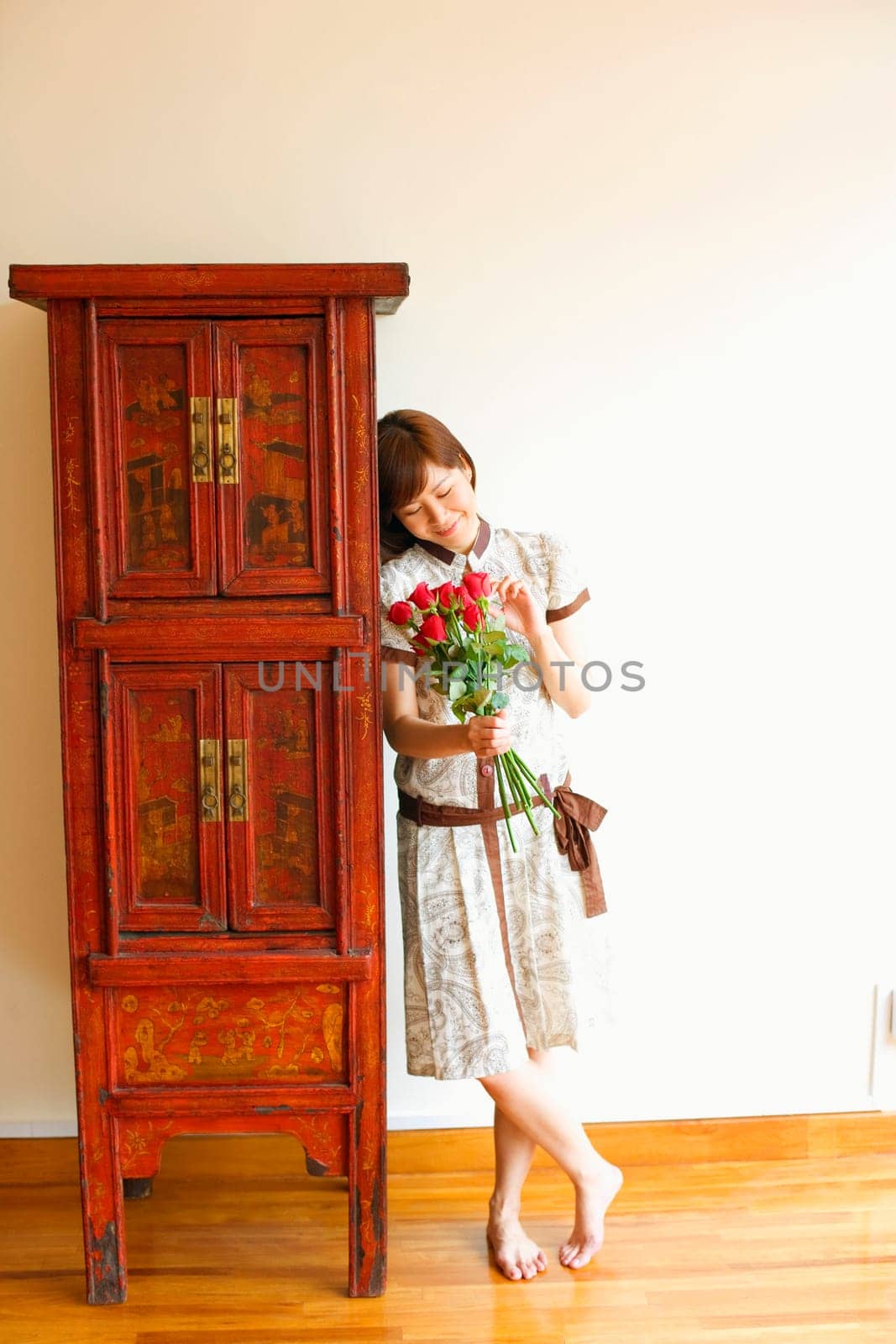 Close-up of a young woman standing near a cabinet and holding a bouquet of red roses