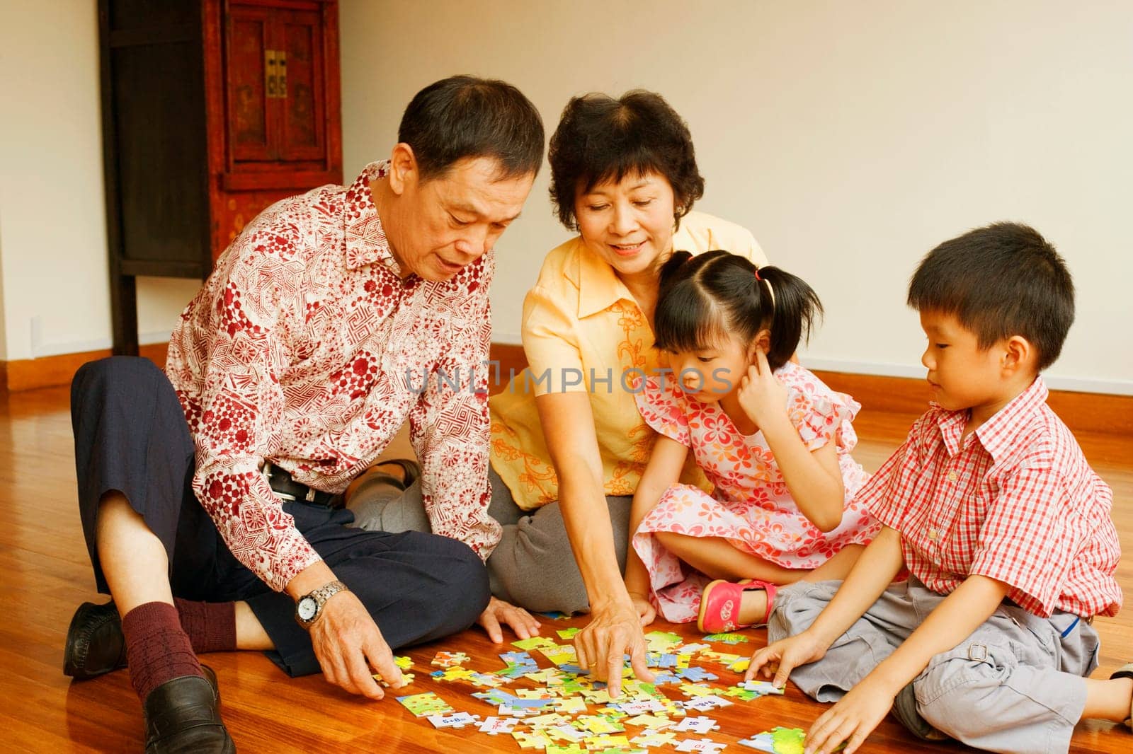 Boy with a girl and their grandparents playing with a jigsaw puzzle