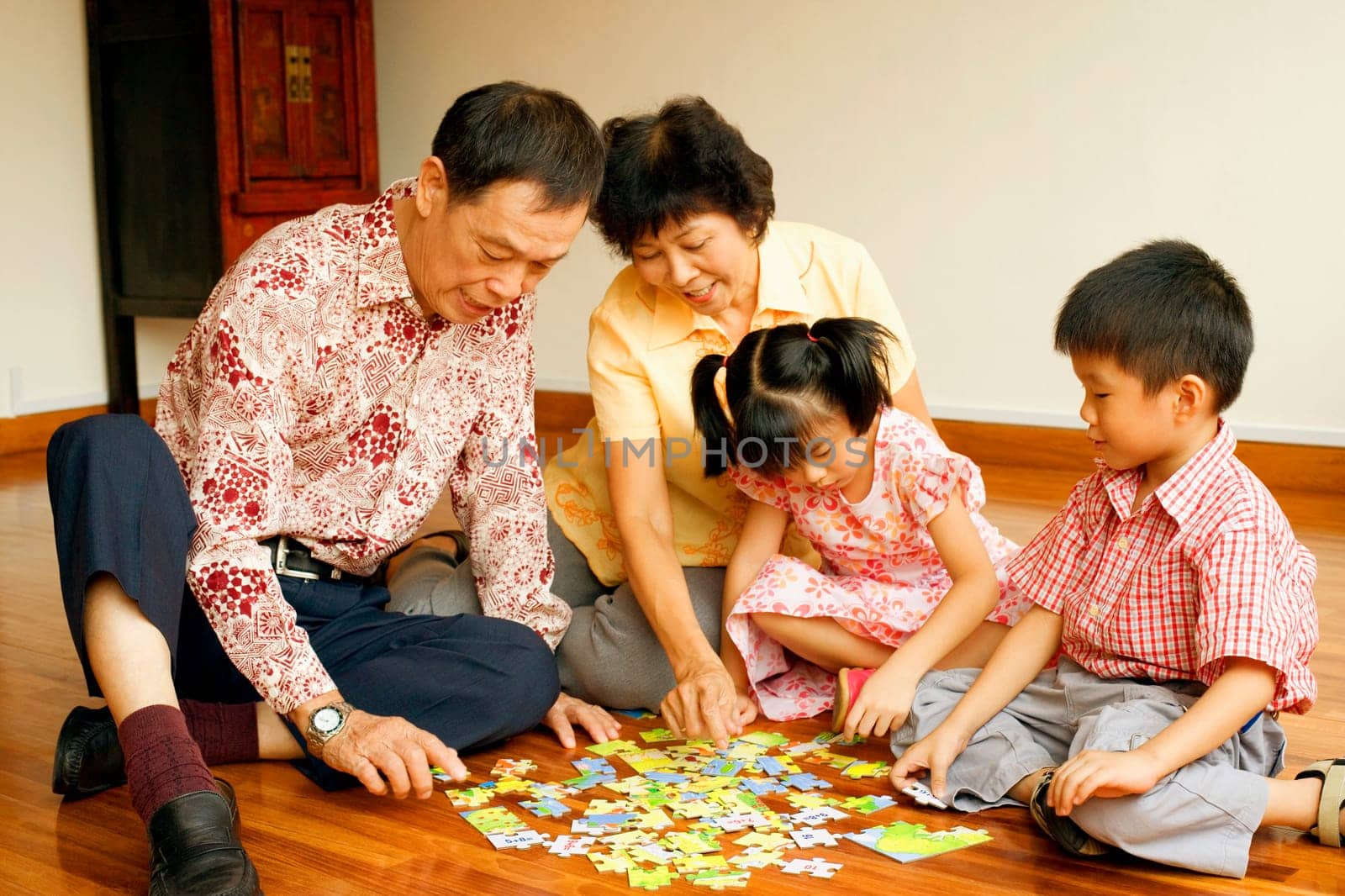 Girl and a boy playing jigsaw puzzle with their grandparents