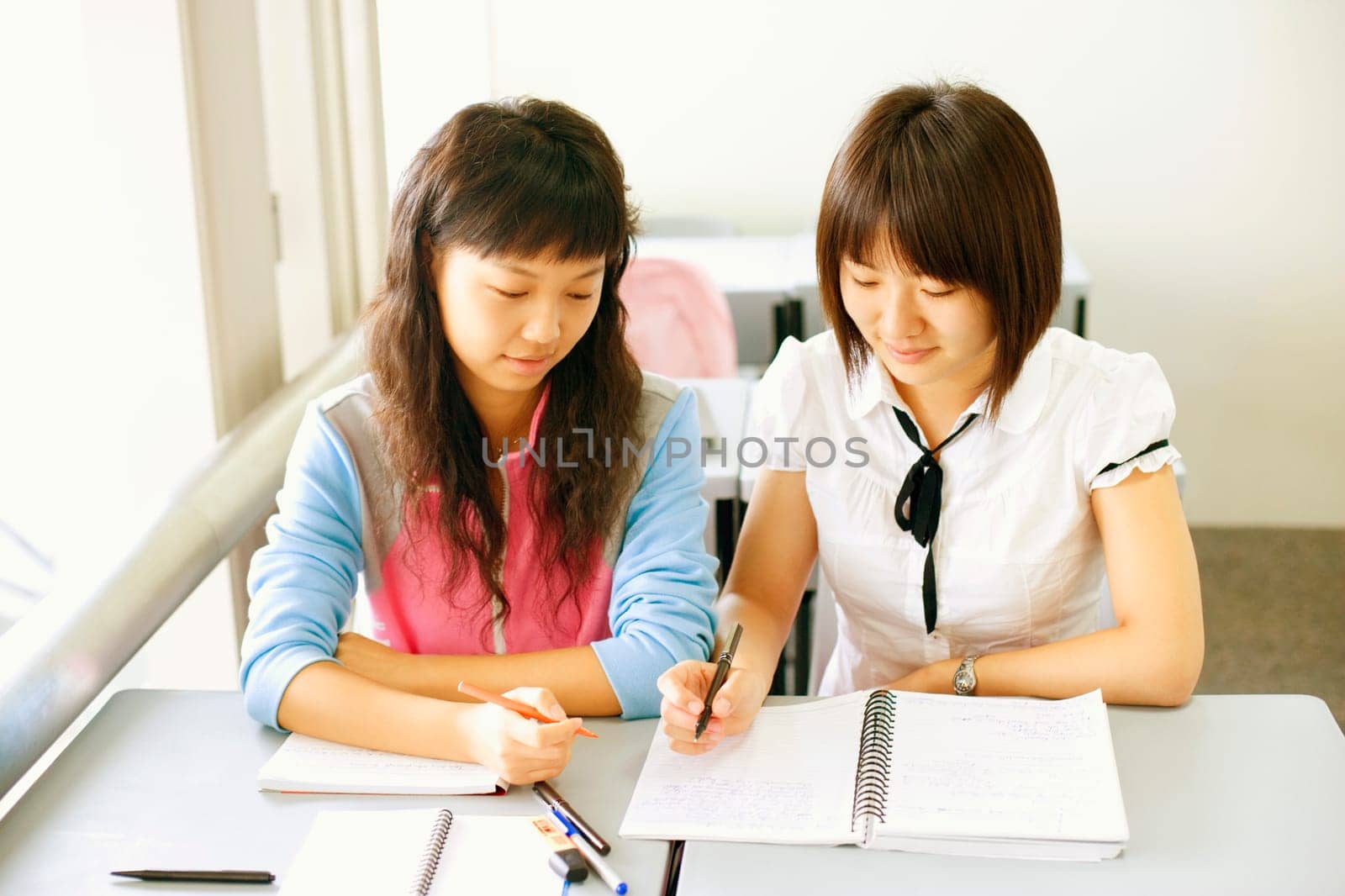 High angle view of two young women holding pens and looking at a spiral notepad