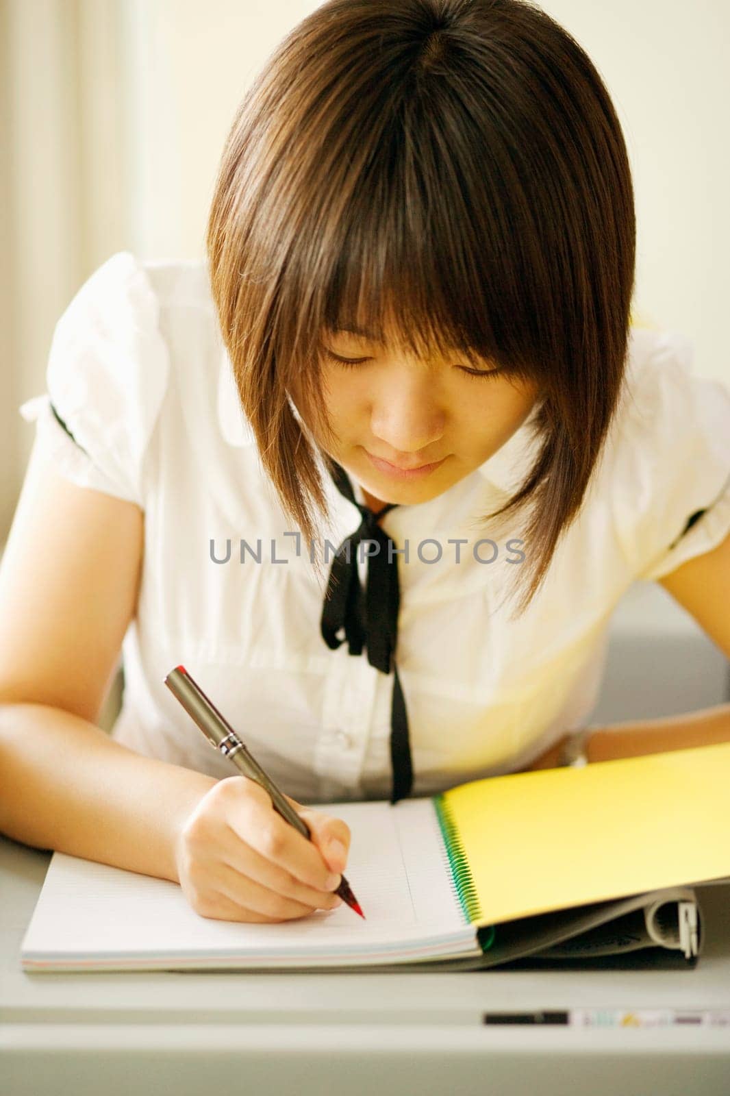 Close-up of a young woman writing on a notepad in a classroom