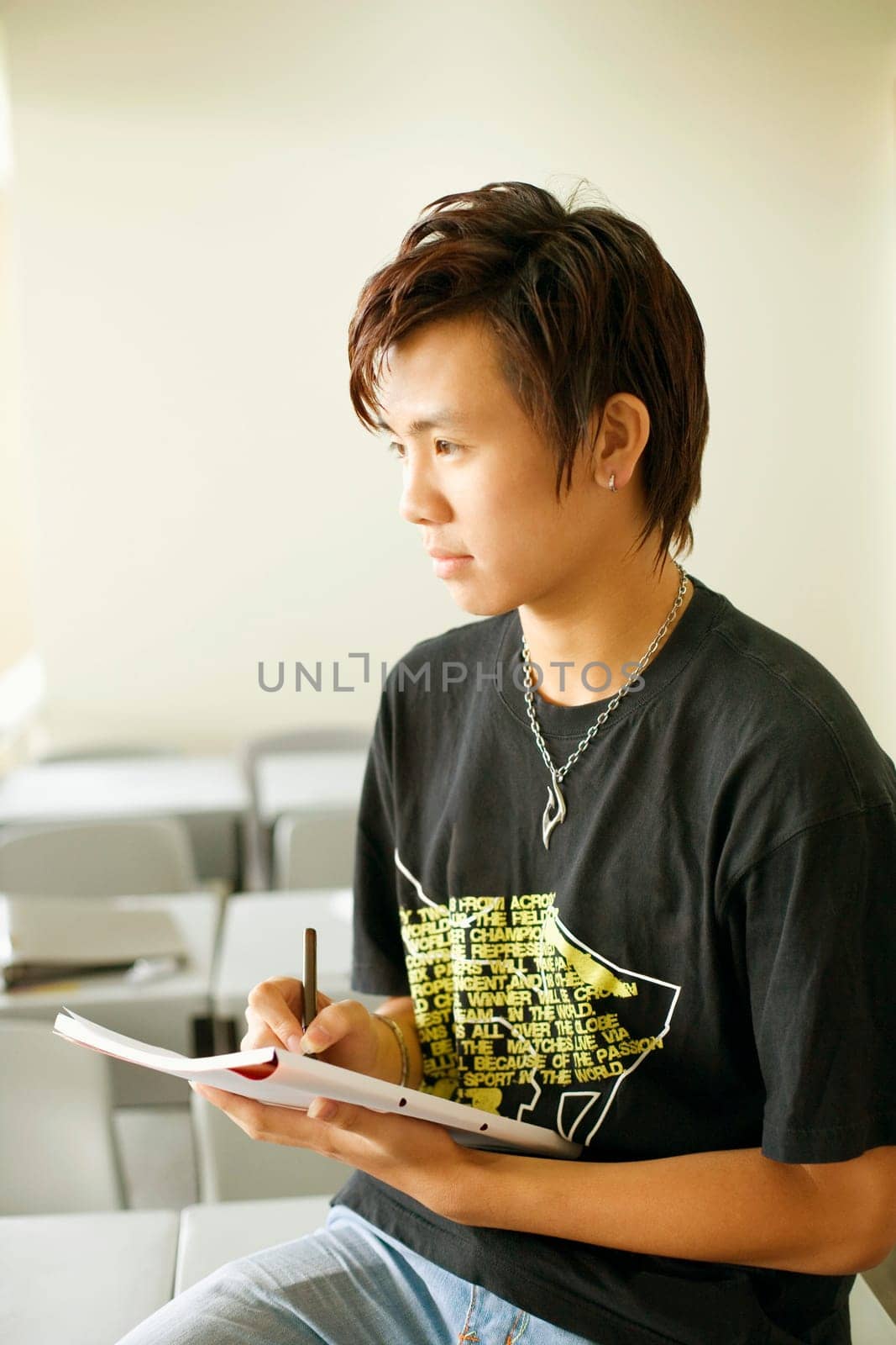 Close-up of a teenage boy writing on a notepad and sitting in the classroom