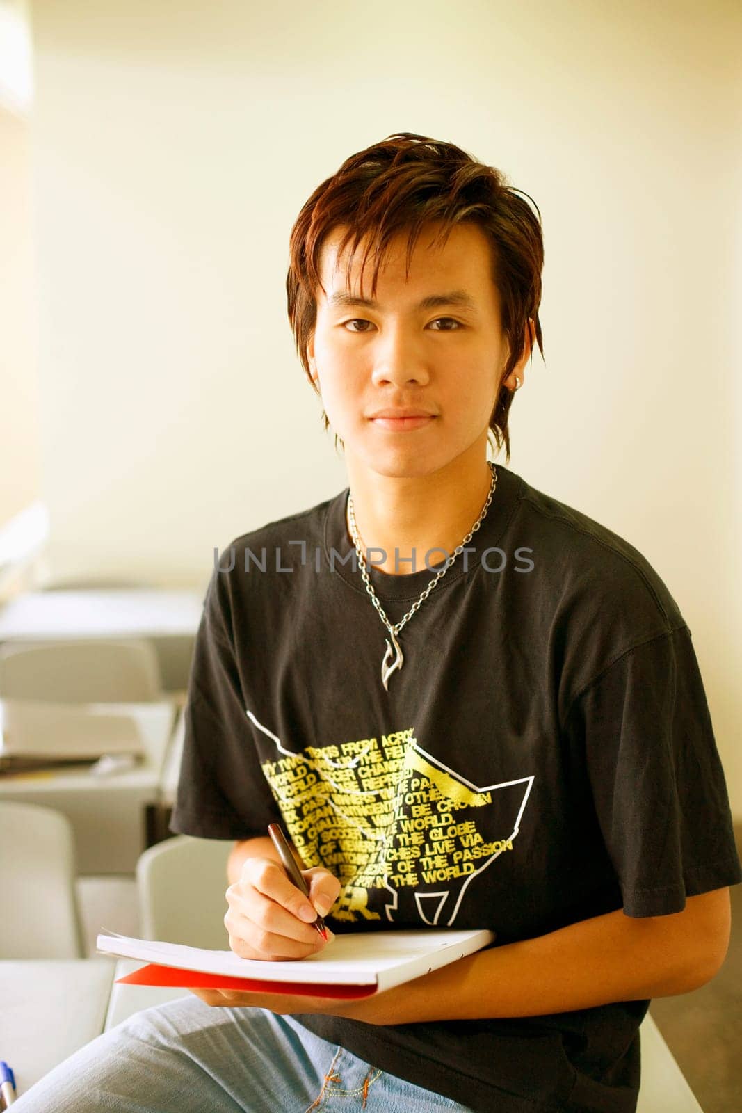 Portrait of a teenage boy holding a pen on a notepad in a classroom