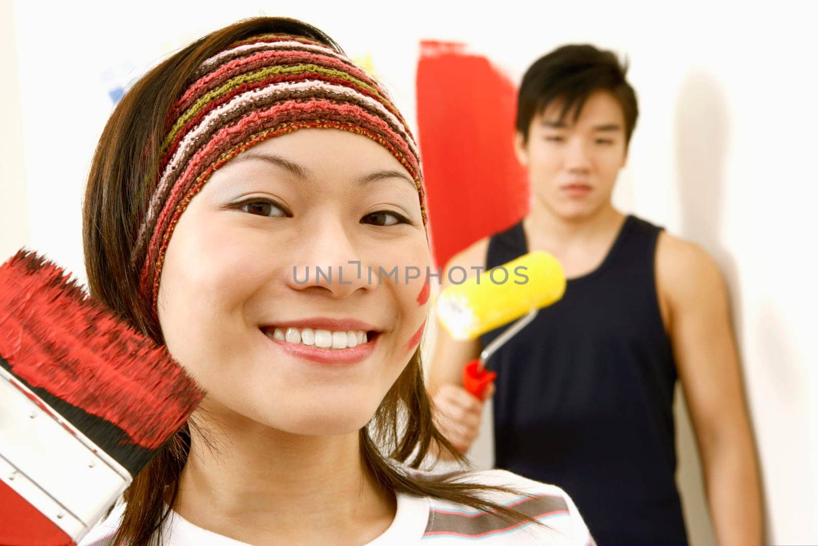 Portrait of a young woman holding a paint brush and a young man standing in the background