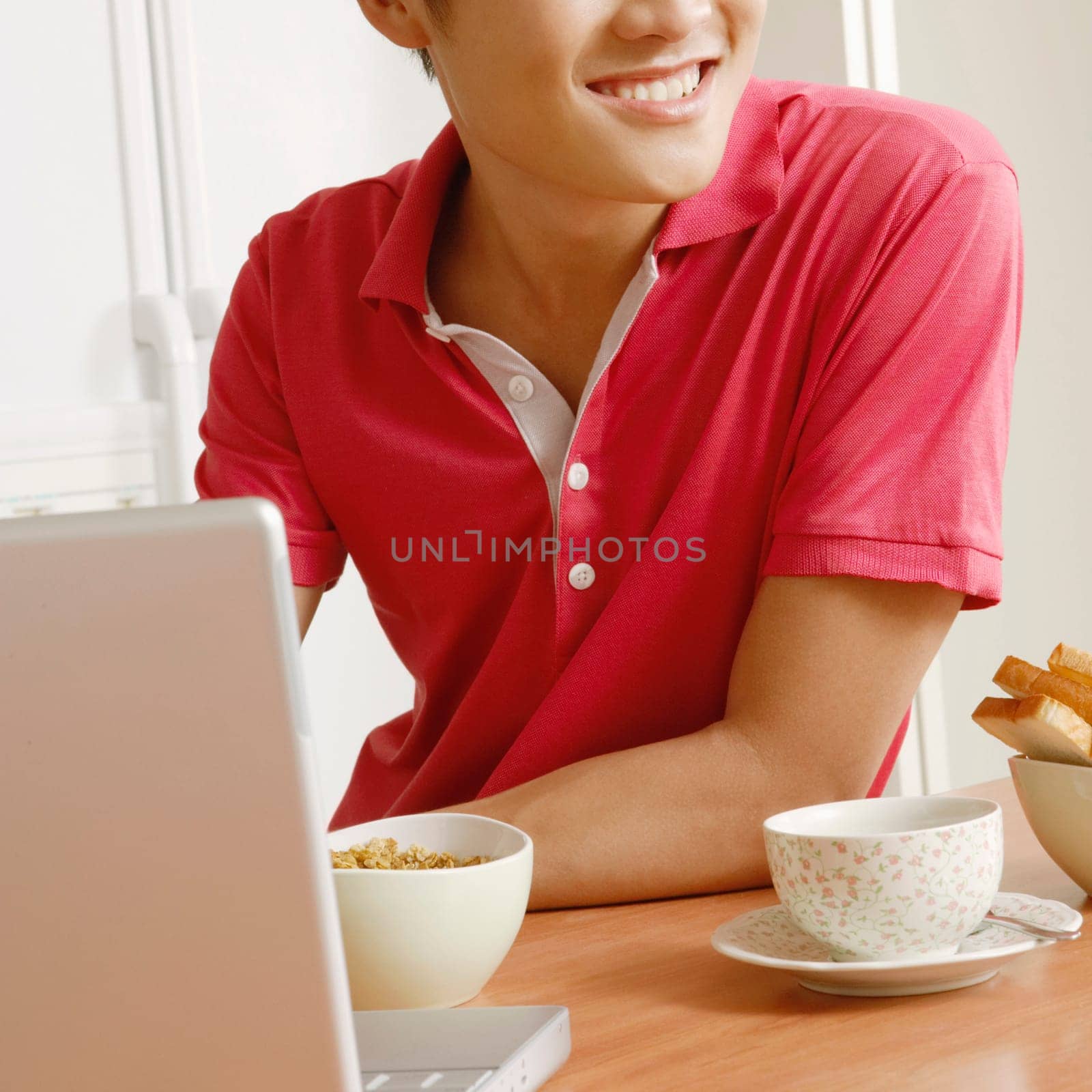 Close-up of a young man smiling in front of a laptop at a kitchen counter