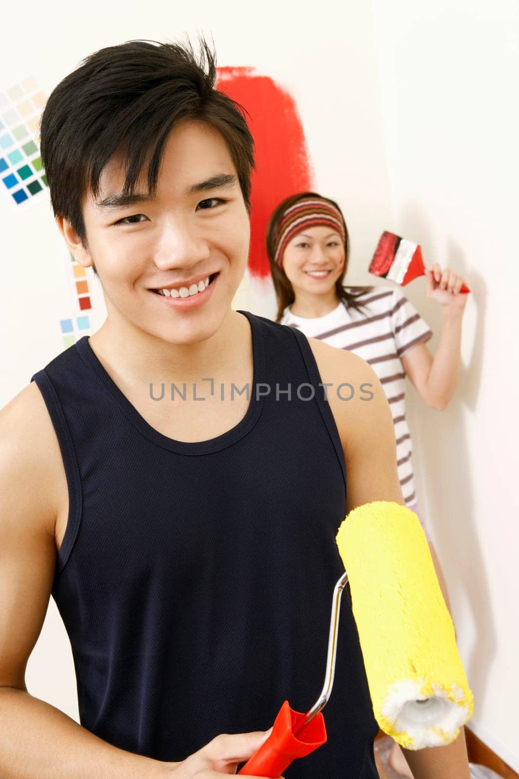 Portrait of a young man holding a paint roller with a young woman standing in the background