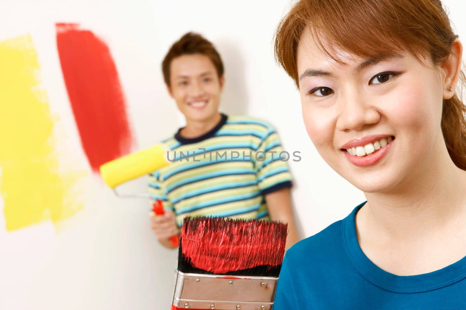Portrait of a young woman holding a paintbrush with a young man standing in the background