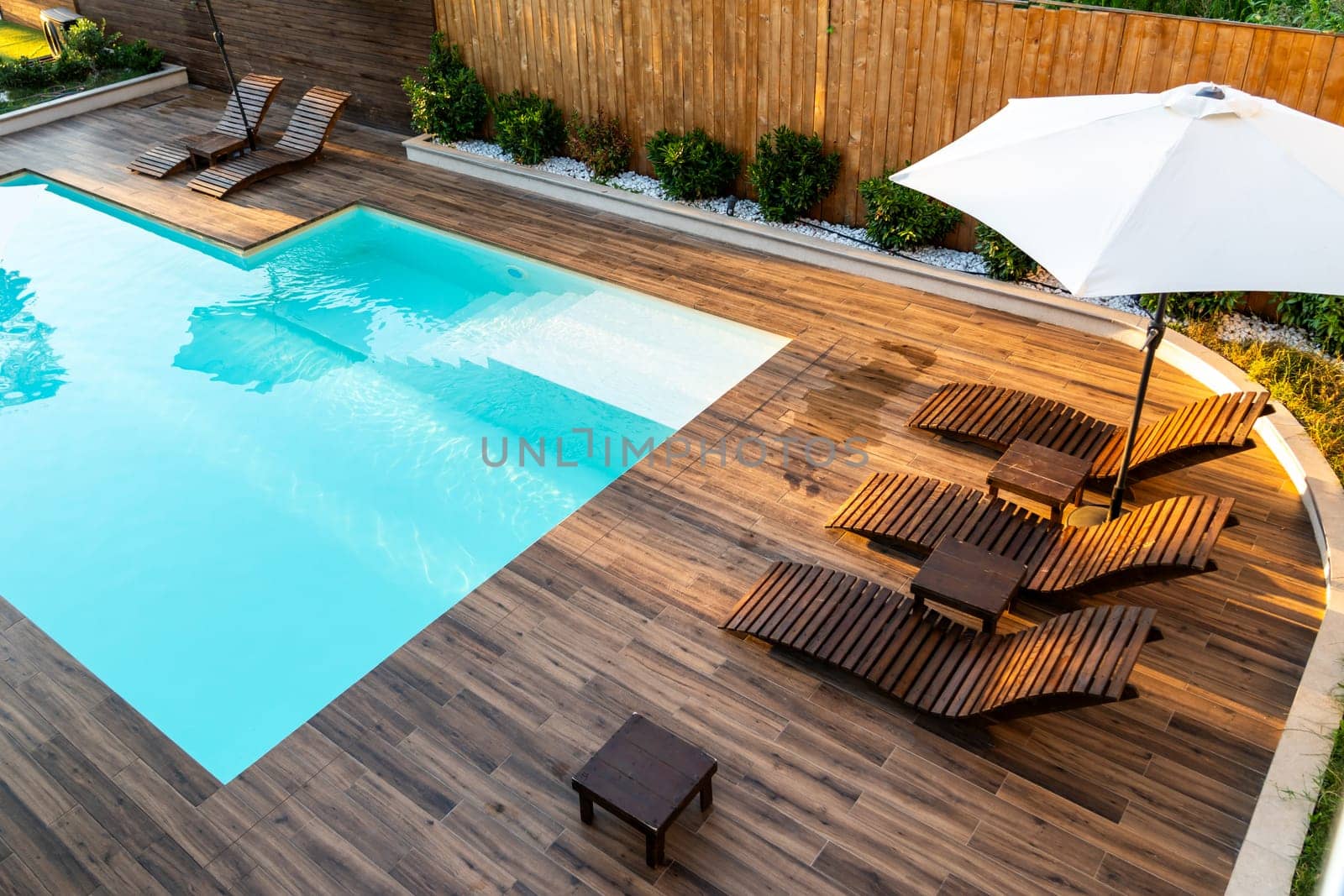 Elegant poolside wooden deck with lounge chairs, umbrella, and turquoise swimming pool in a serene backyard