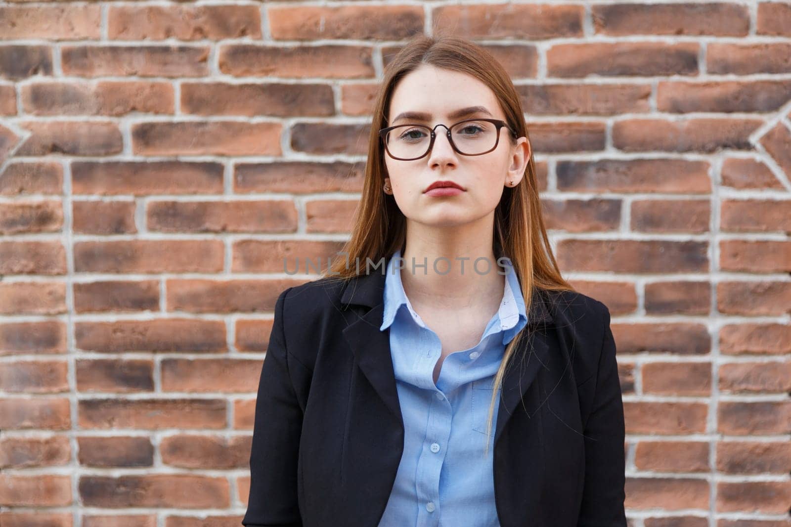Portrait young office worker woman in suit and eyeglasses on brick wall background standing outdoor. Zoomer girl street lifestyle portrait
