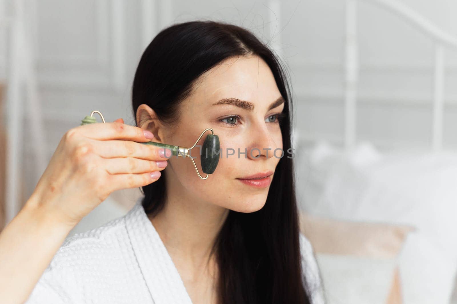 Beautiful european woman uses jade roller to massage her face. Spa self beauty procedure