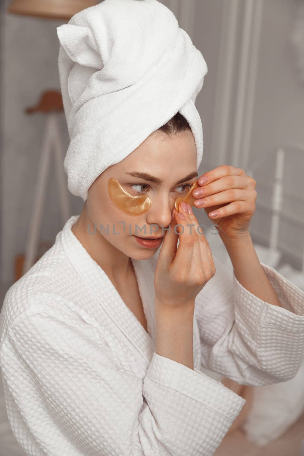 Pretty european girl applying golden collagen patches under her eyes. Woman facial treatment. Cosmetology, beauty and spa