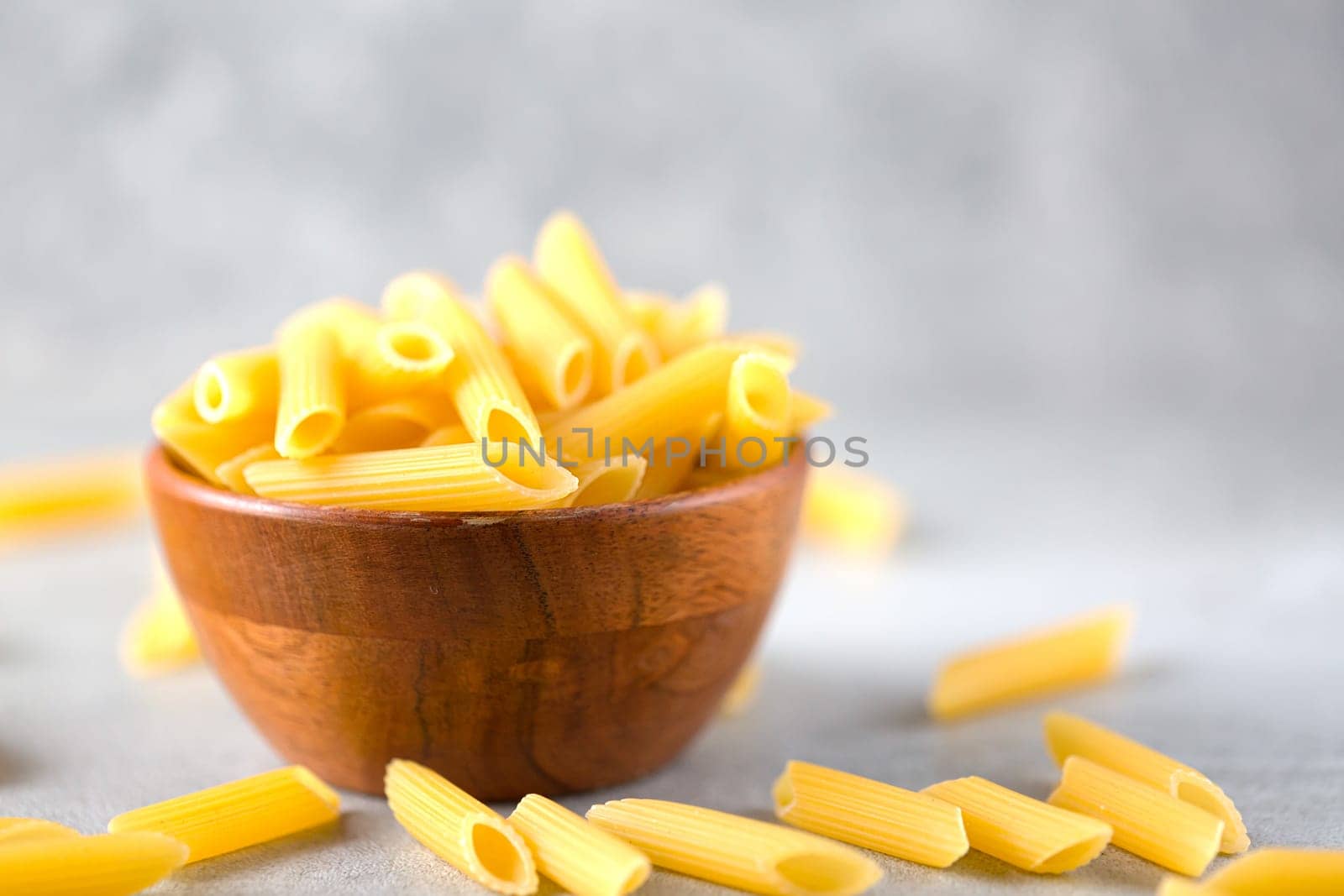 Uncooked yellow pasta in a wooden bowl on gray table. Selective focus. Italian food concept. Copy space