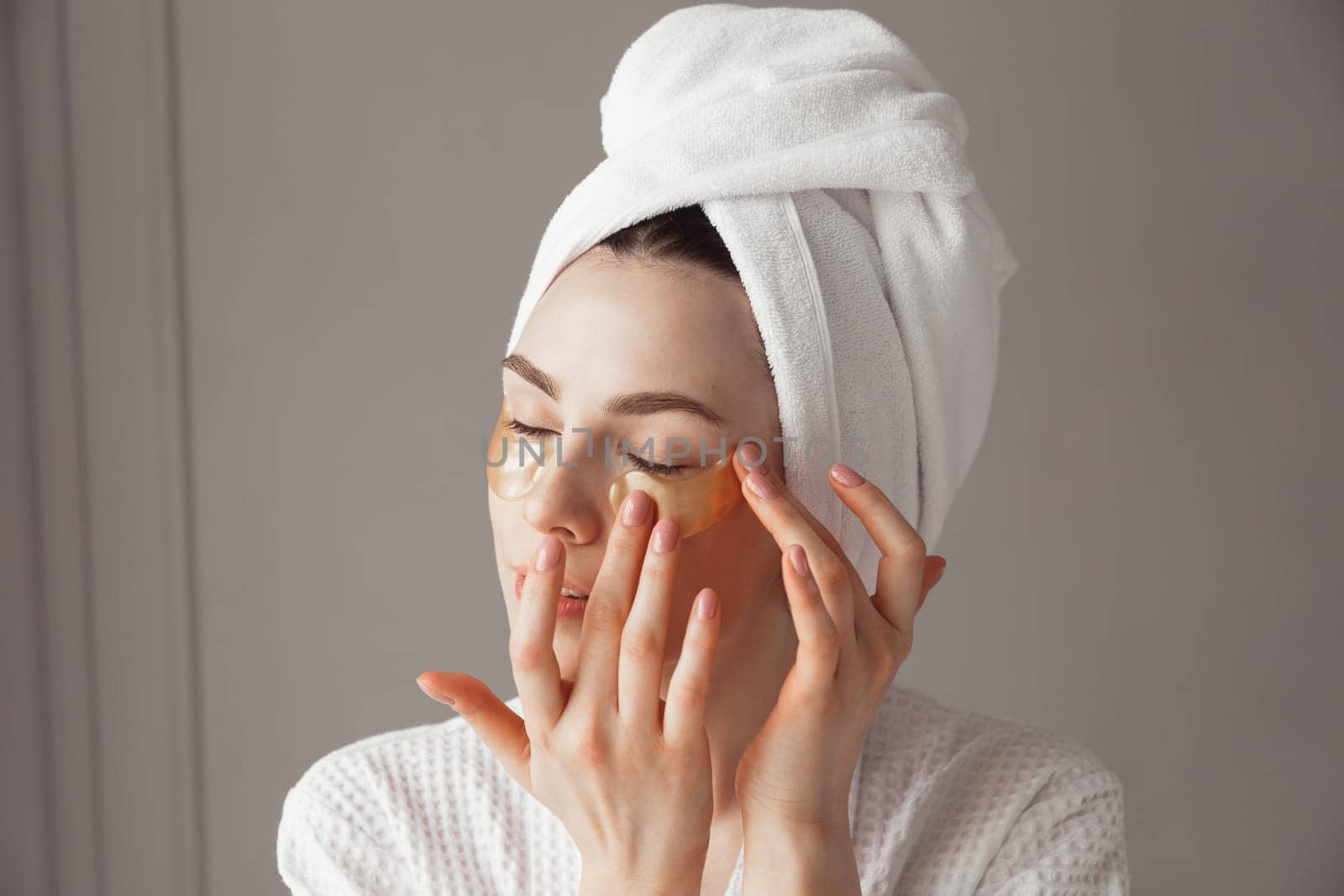 Pretty european girl applying golden collagen patches under her eyes. Woman facial treatment. Cosmetology, beauty and spa